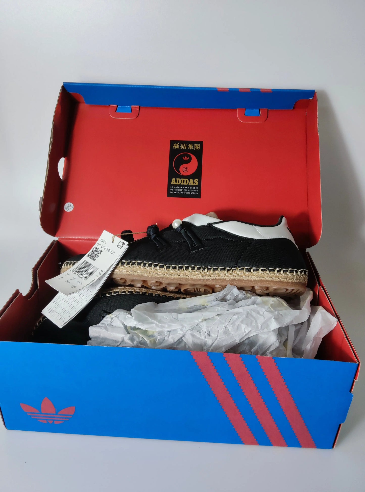 Espadrilles noires par Adidas, dans sa boîte rouge et bleue, avec motif à chevrons sur le côté.