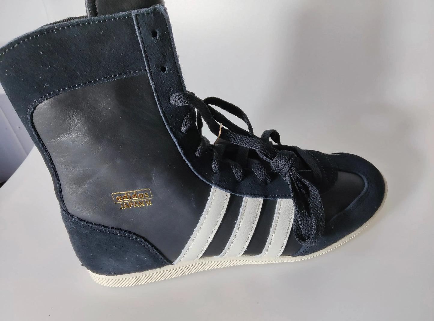 Baskets montantes noires en cuir par Adidas, avec trois bandes blanches sur le côté et lacets noirs.