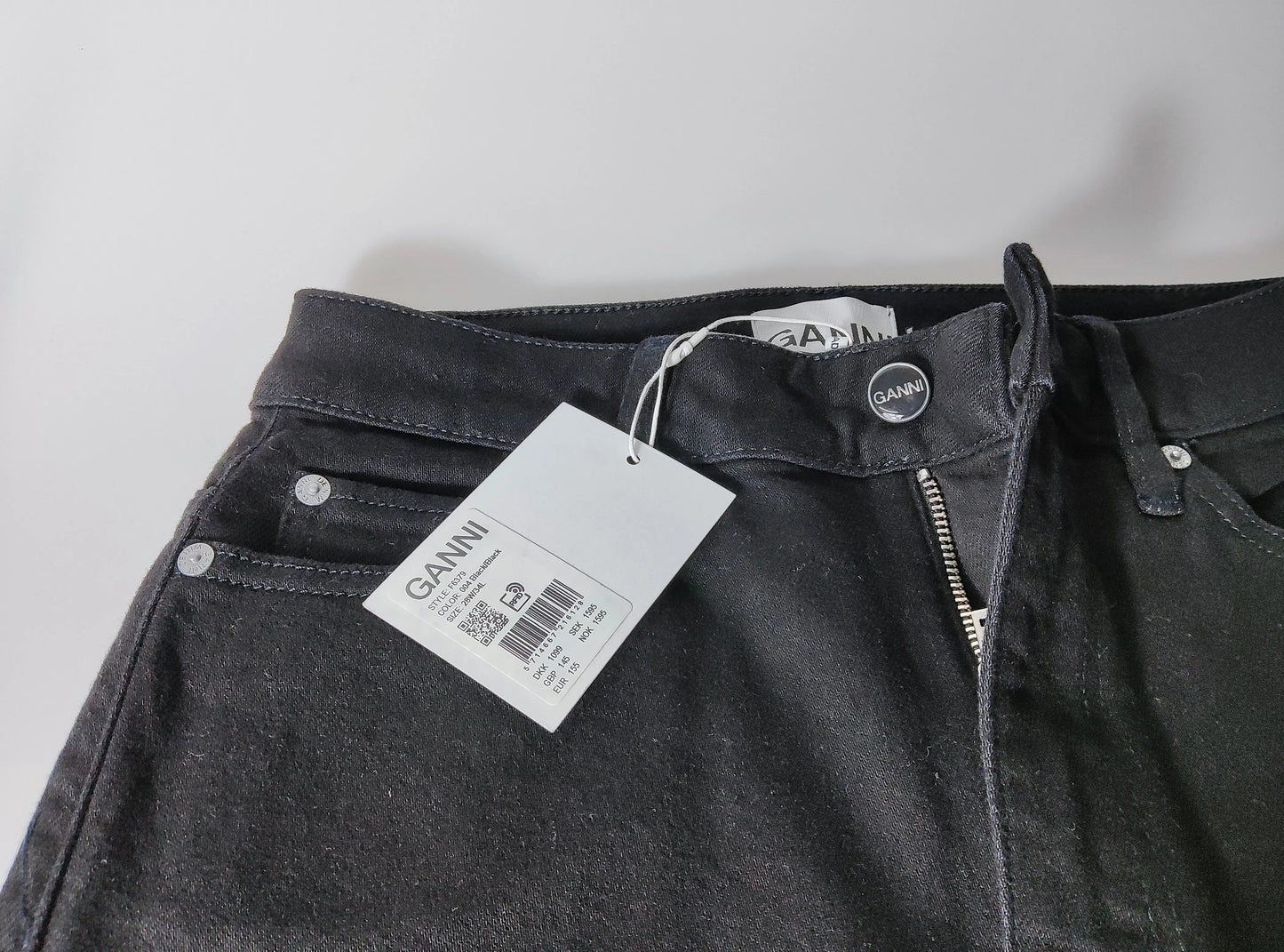 Jean noir taille haute cropped de Ganni, avec une fermeture éclair et une étiquette de prix.