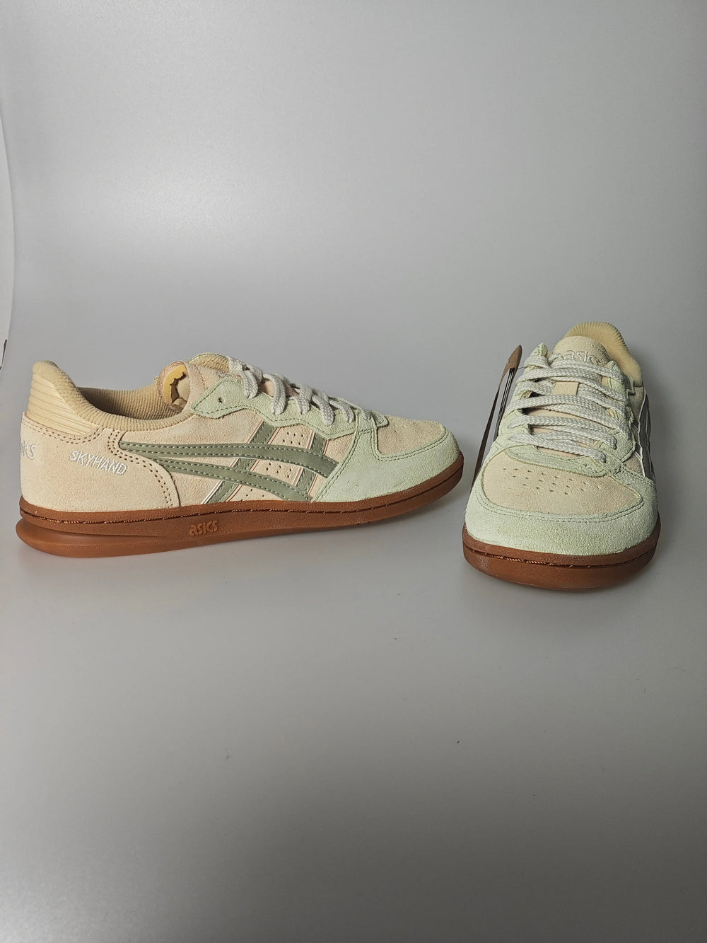 Chaussure de basket beige en daim, de Asics, avec des rayures vertes et une semelle marron.