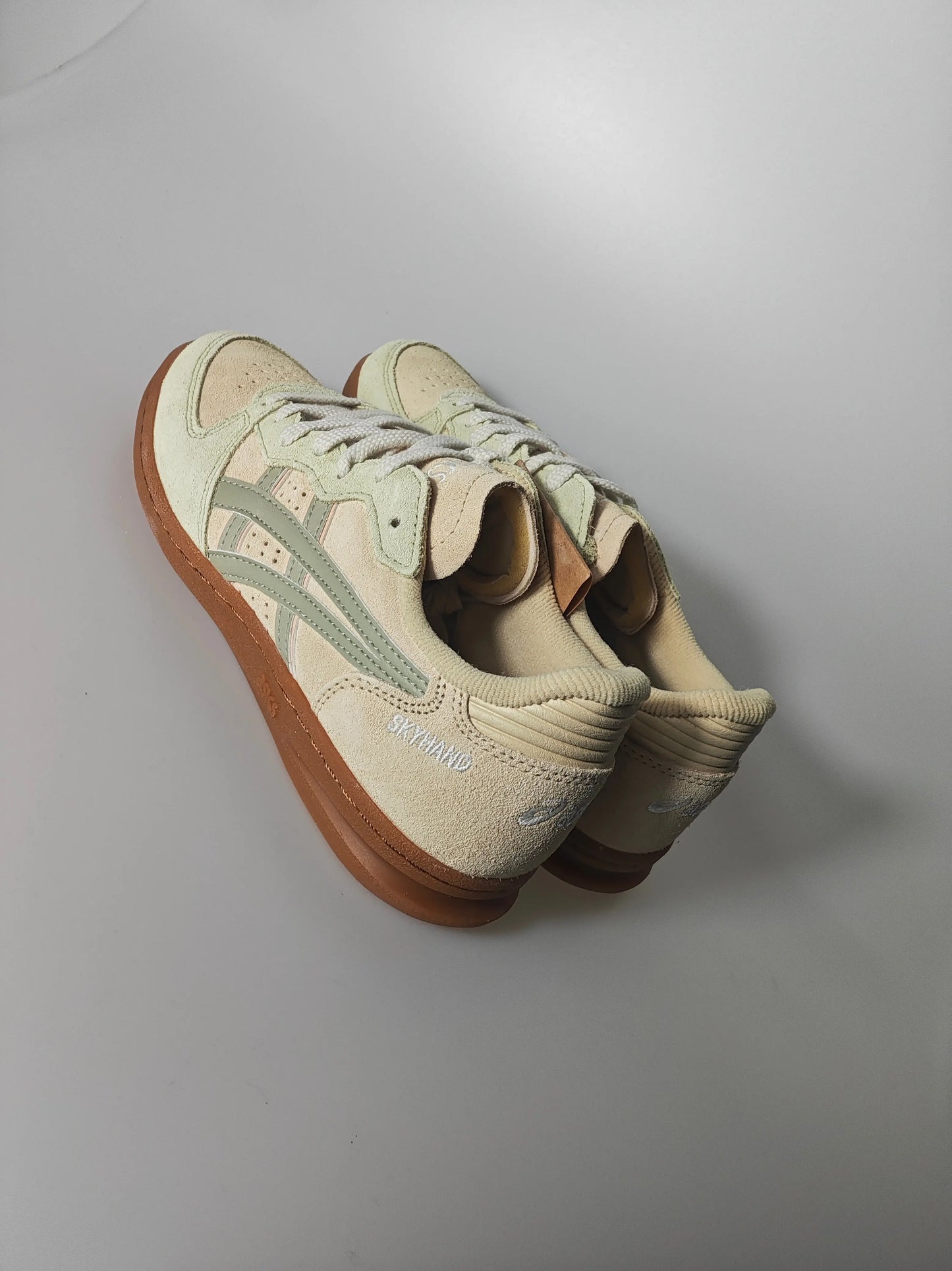 Chaussures de basket-ball beiges par Asics, avec des détails verts et une semelle extérieure marron.