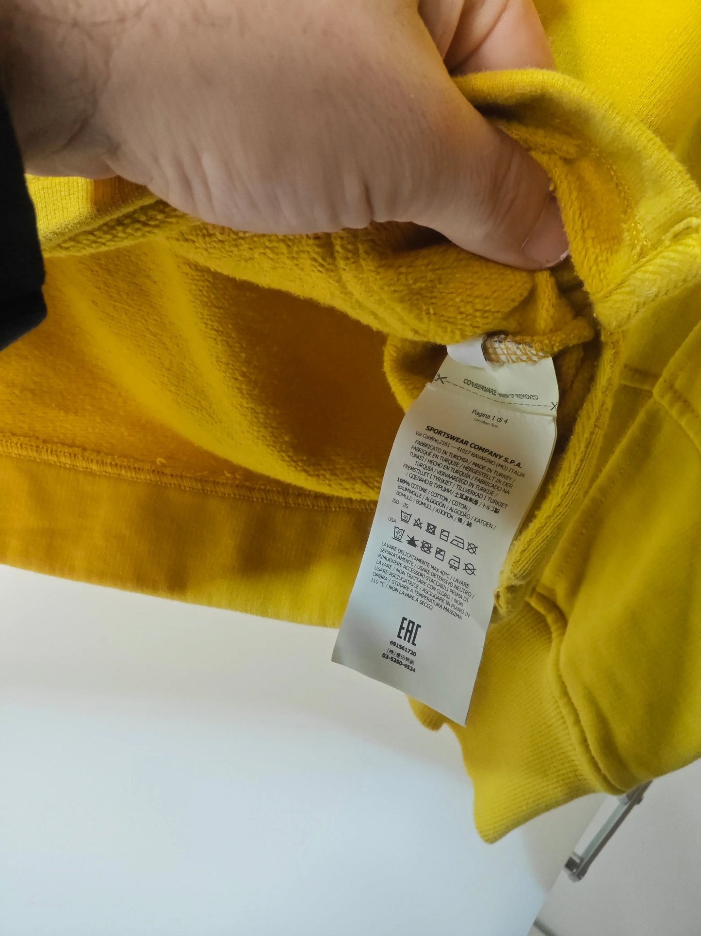 Sweat jaune moutarde taille S de Stone Island, présentant une étiquette d'entretien en gros plan.