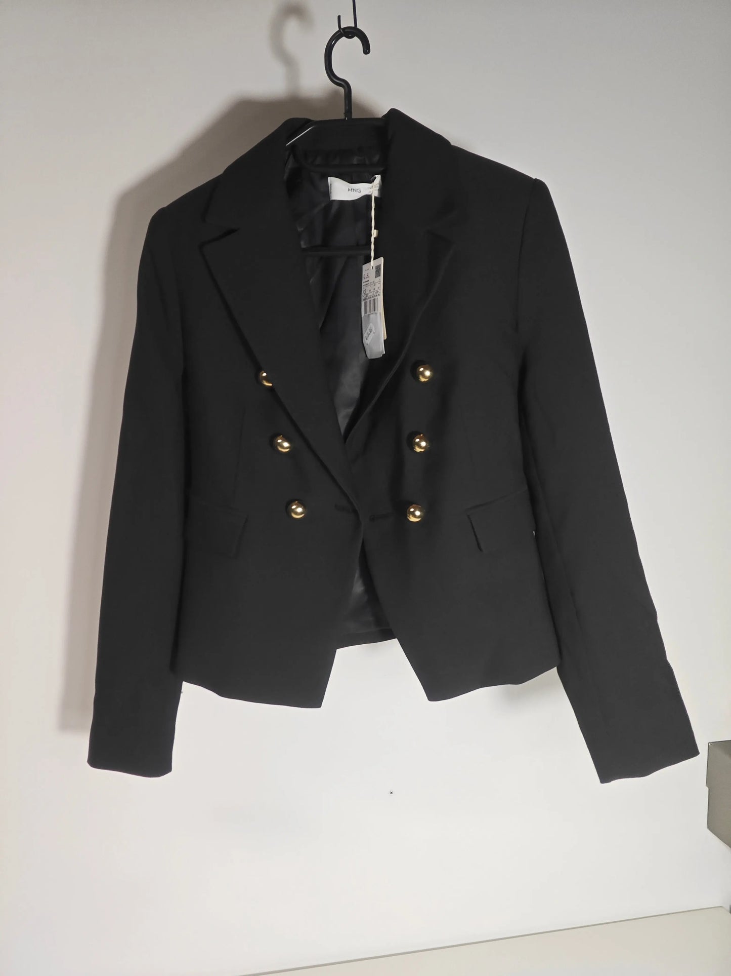 Blazer noir cintré de Mango avec boutons dorés, suspendu sur un cintre.