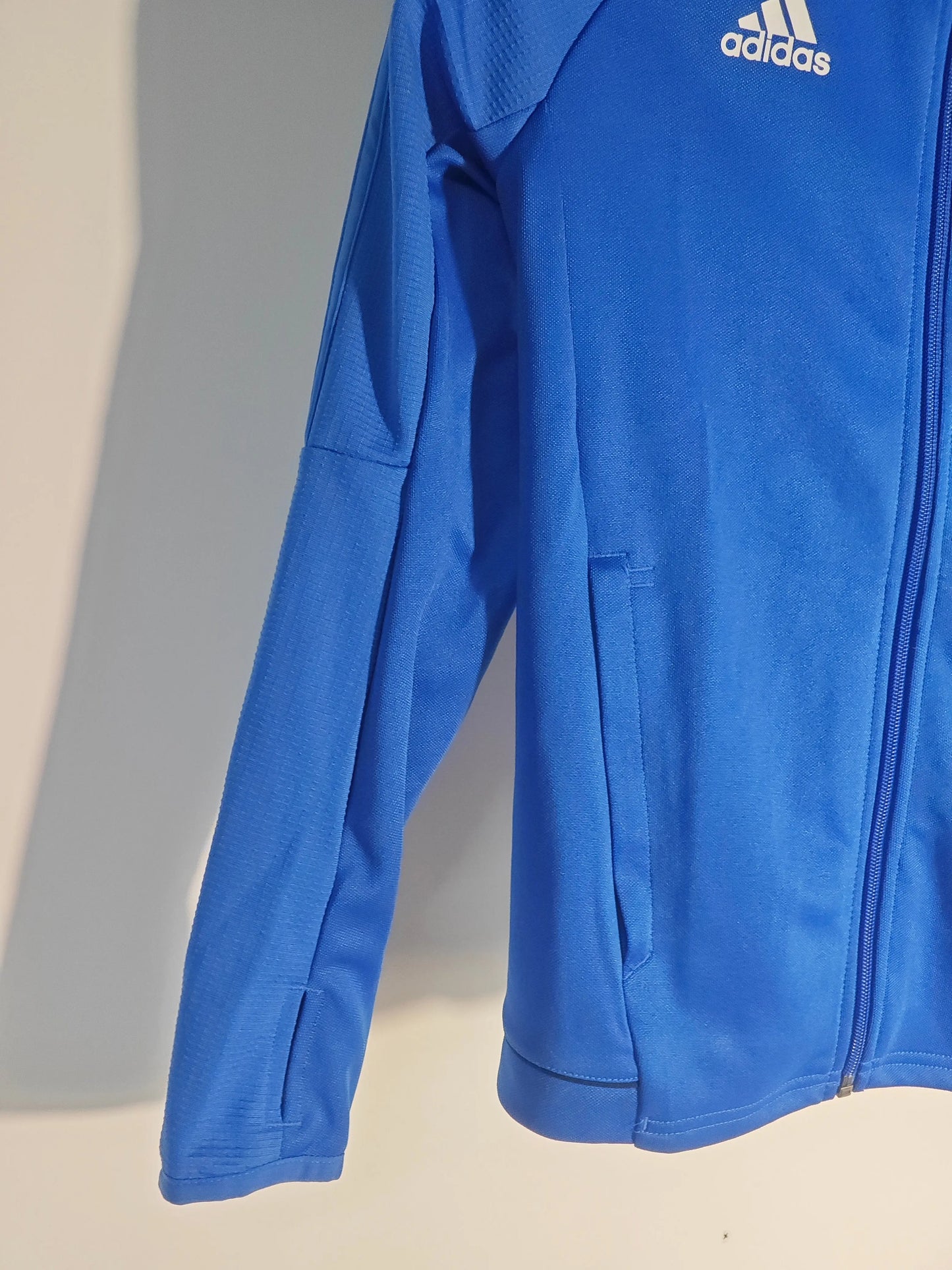 Veste de sport bleue de Adidas, avec fermeture éclair et détail texturé sur l'épaule.