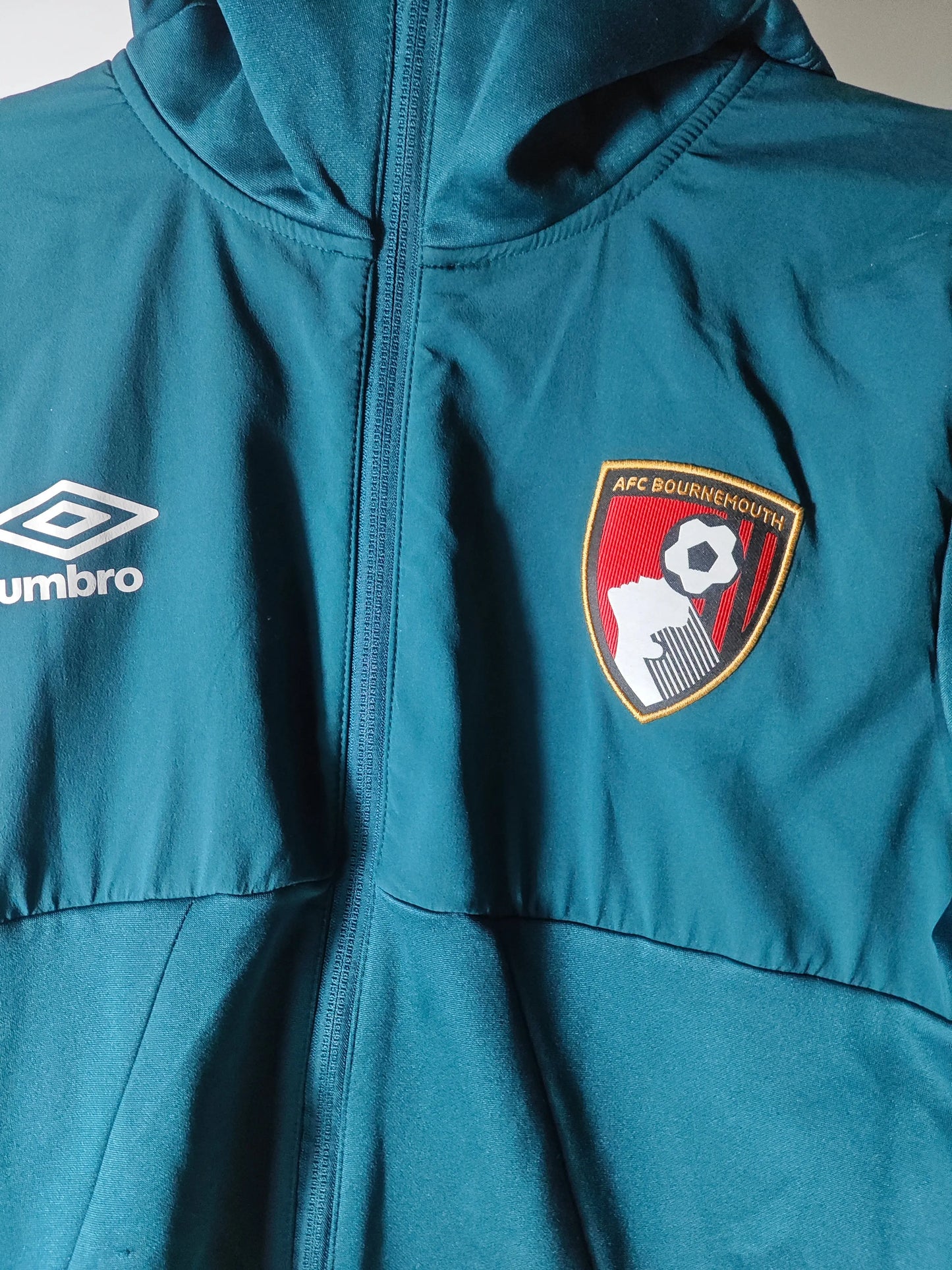Veste de sport turquoise par Umbro, avec l'écusson AFC Bournemouth sur la poitrine et une fermeture éclair.