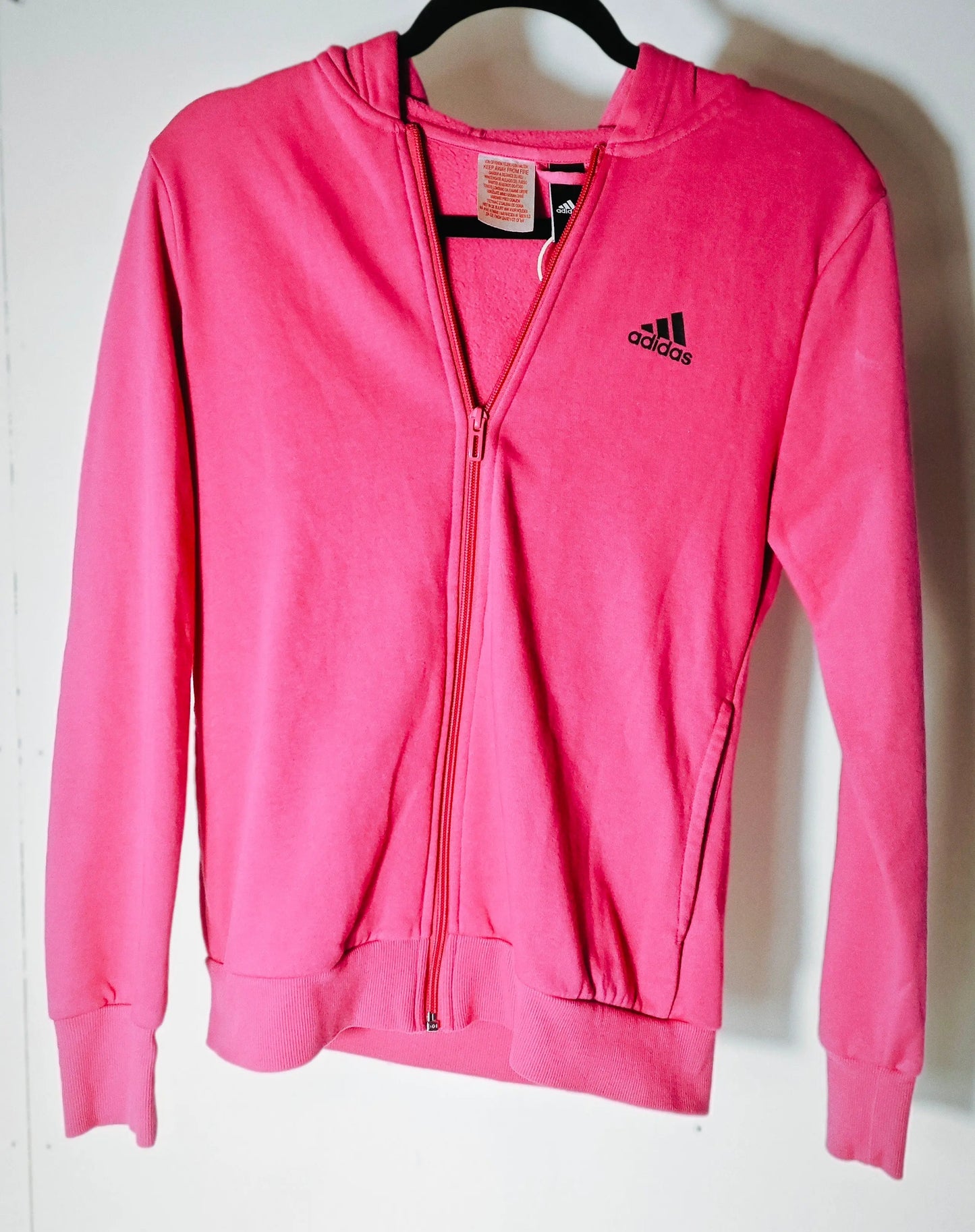 Veste de survêtement à capuche rose fuchsia d'Adidas, avec logo noir sur la poitrine et fermeture éclair intégrale.