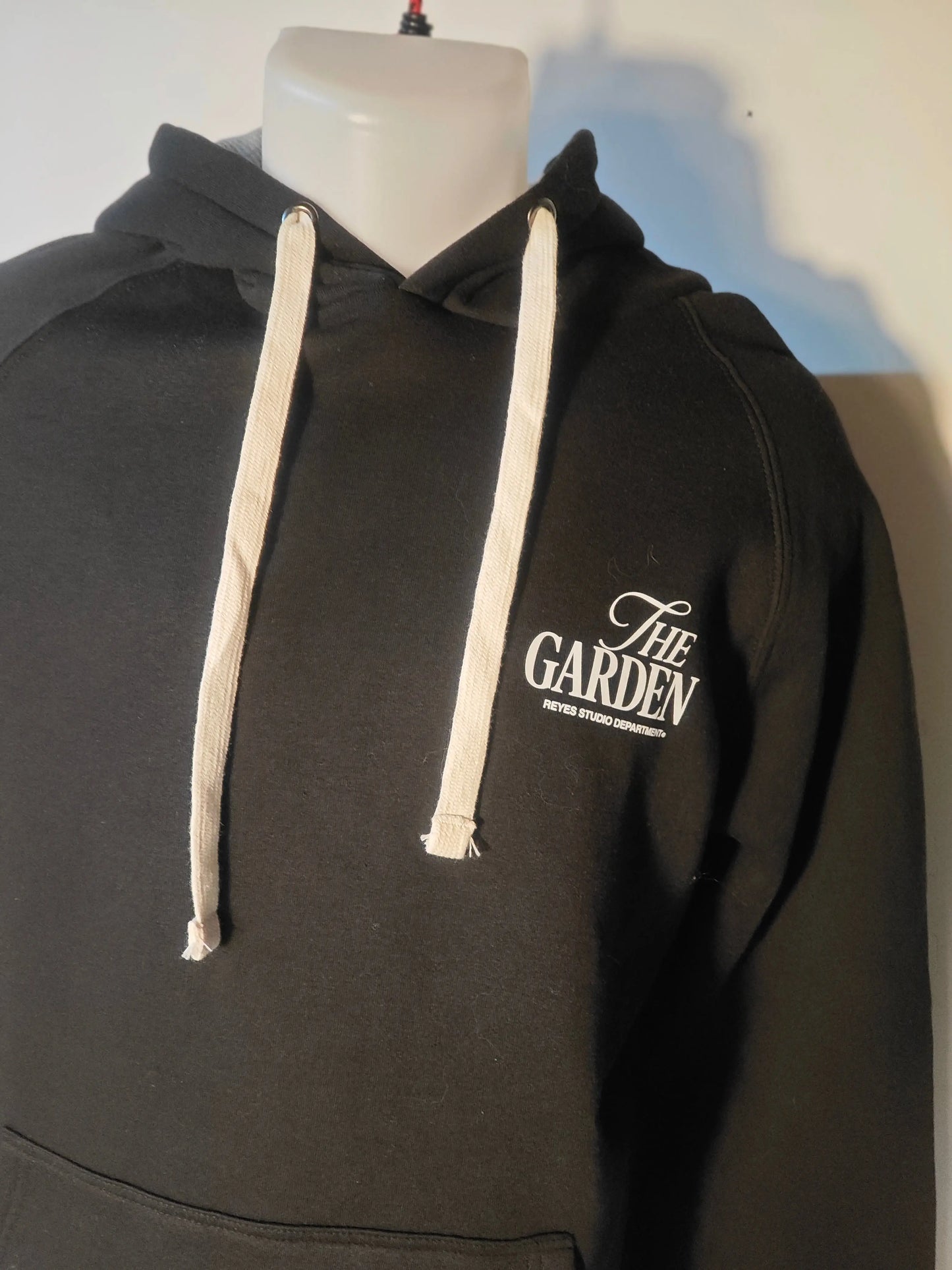 Hoodie noir de The Garden by Reyes Studio Department, avec cordon blanc et logo imprimé.
