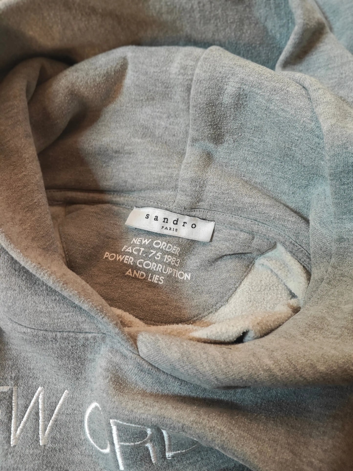 Sweat à capuche gris de Sandro, avec inscription "New Order Fact. 75 1983 Power Corruption and Lies" et capuche doublée.