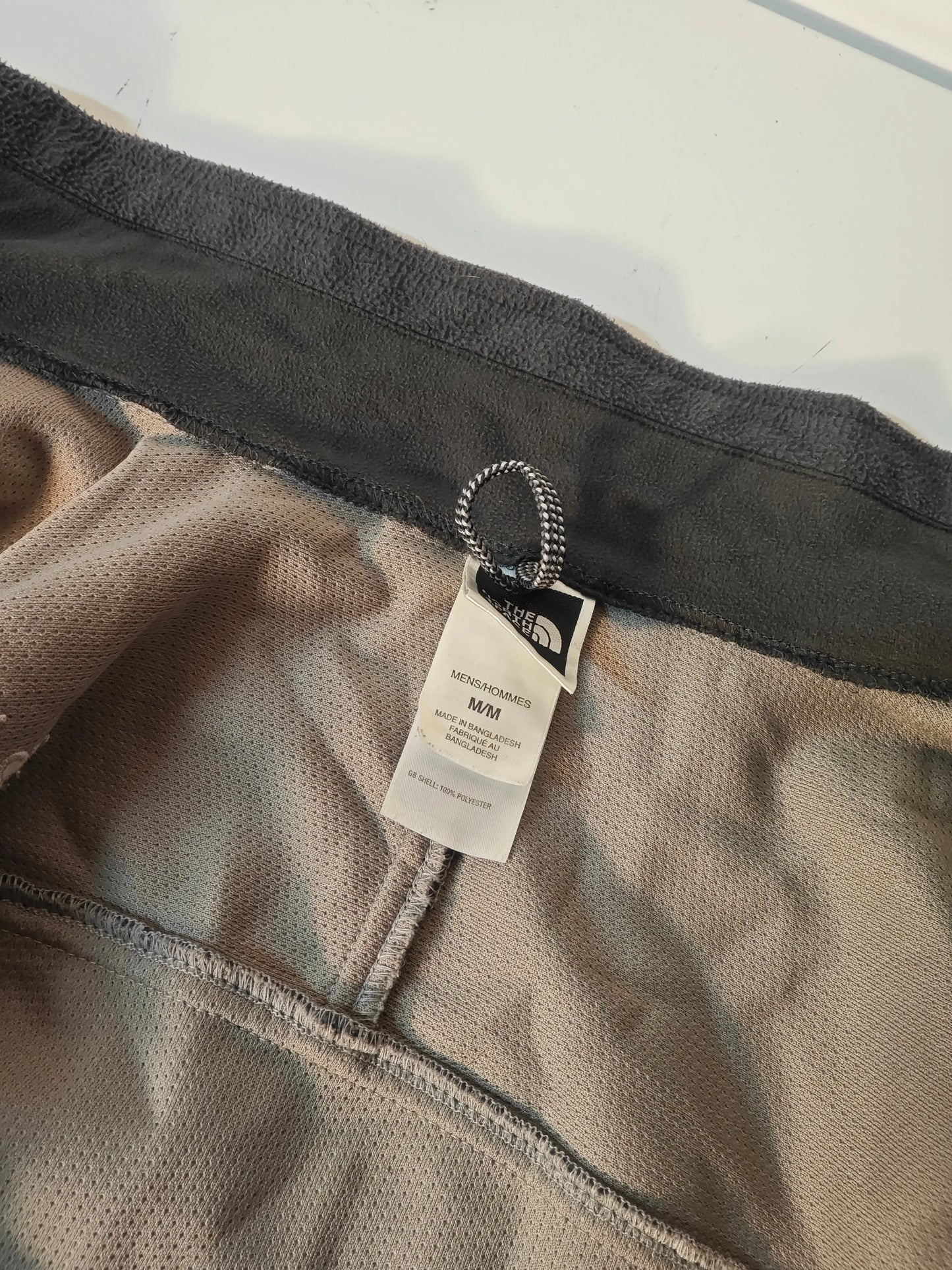 Polaire homme beige de The North Face, avec bordure grise en polaire et étiquette de taille visible.