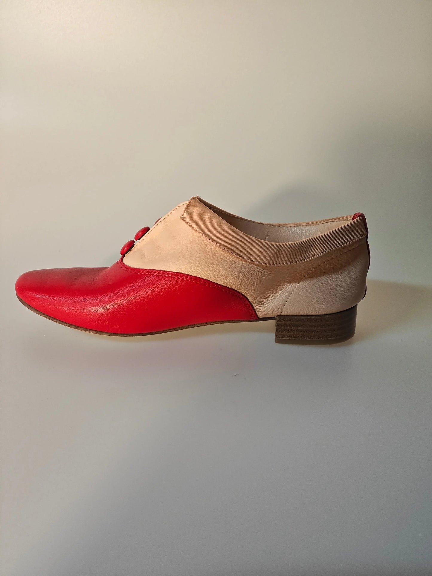 Richelieu en cuir rouge et nude de Repetto, avec petits boutons rouges décoratifs.