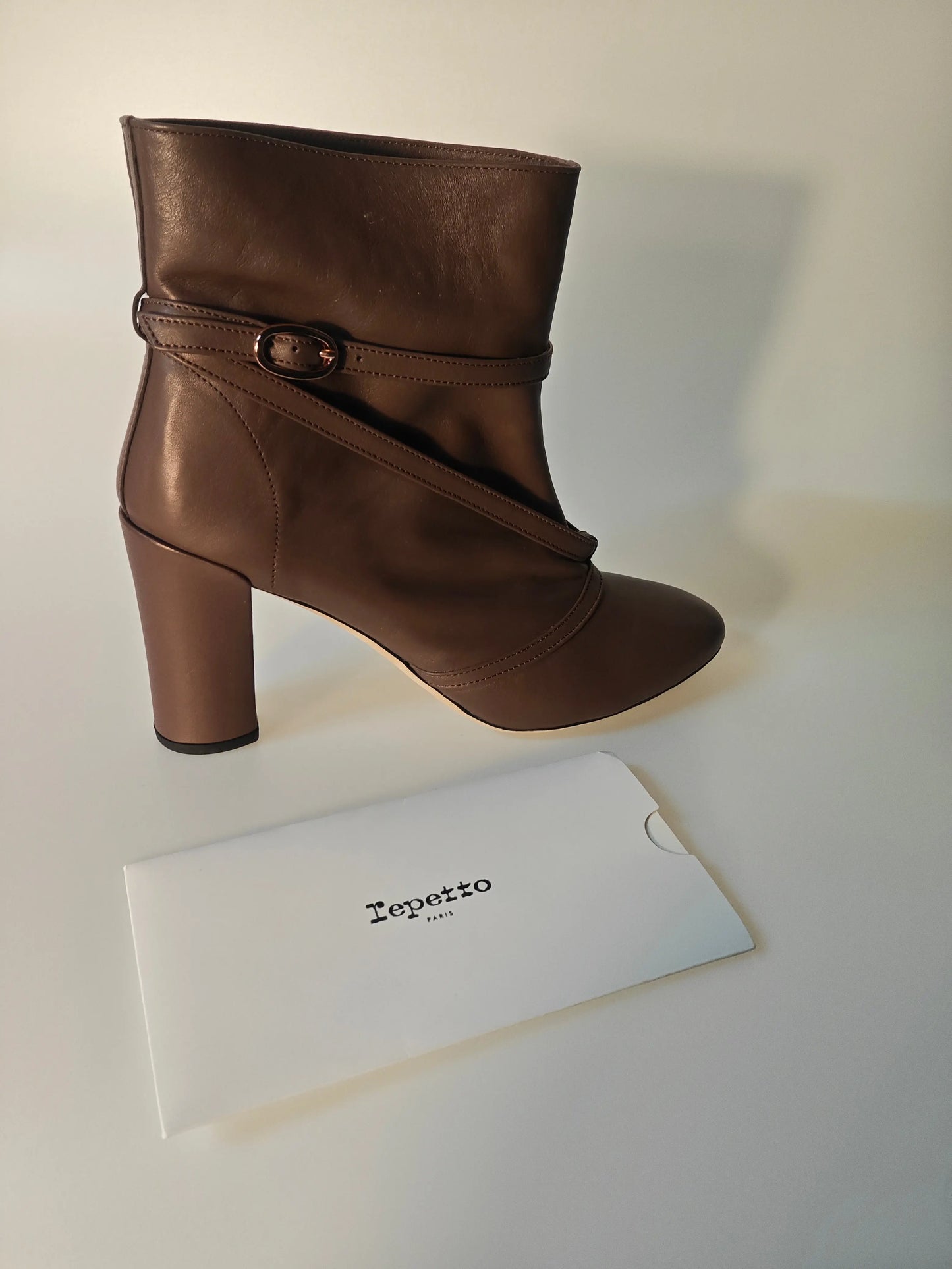 Bottines marron en cuir Repetto avec une bride à boucle, présentées à côté de leur emballage.
