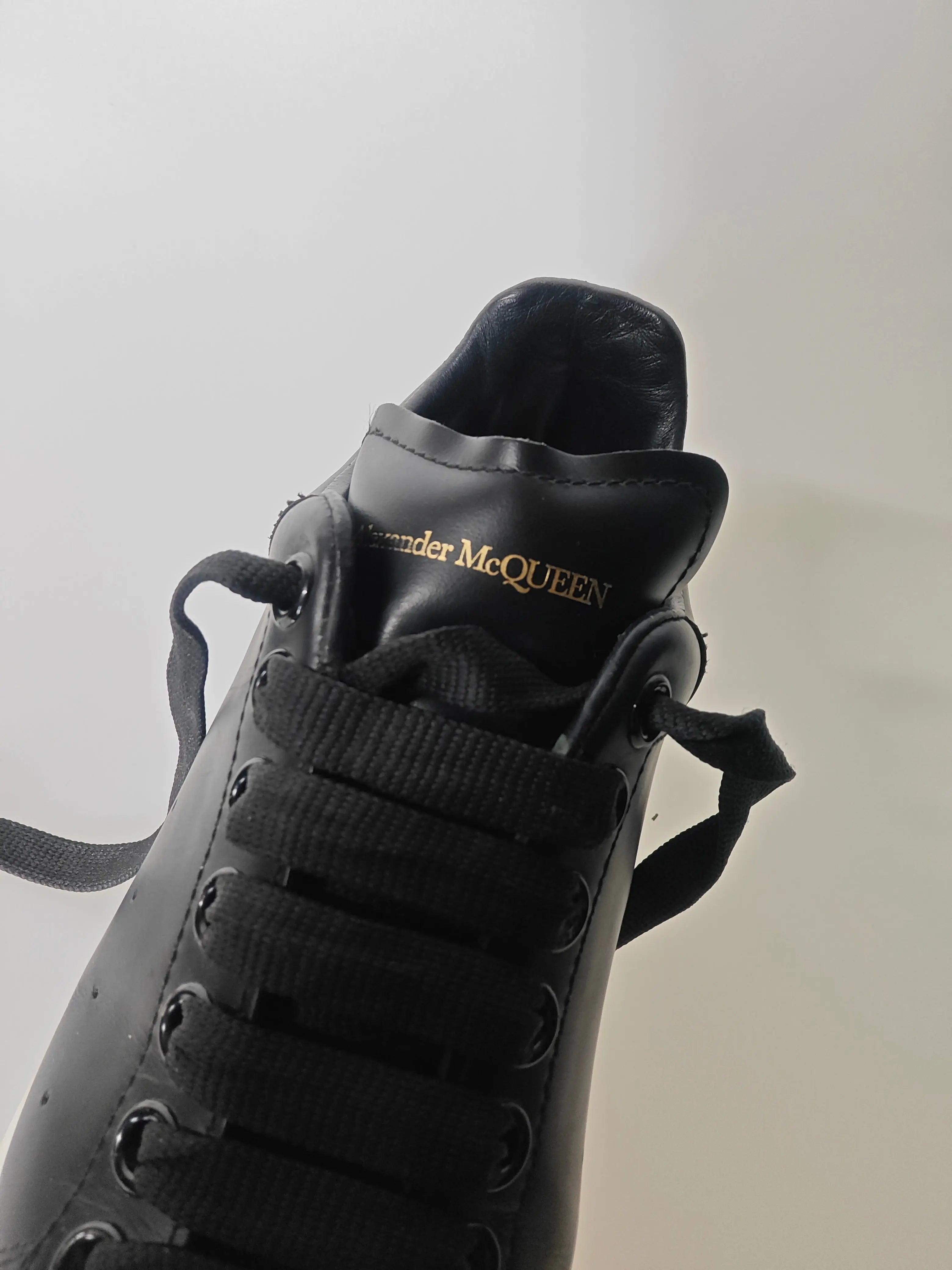 Chaussures en cuir noir de Alexander McQueen, avec lacets noirs et logo doré sur le col.
