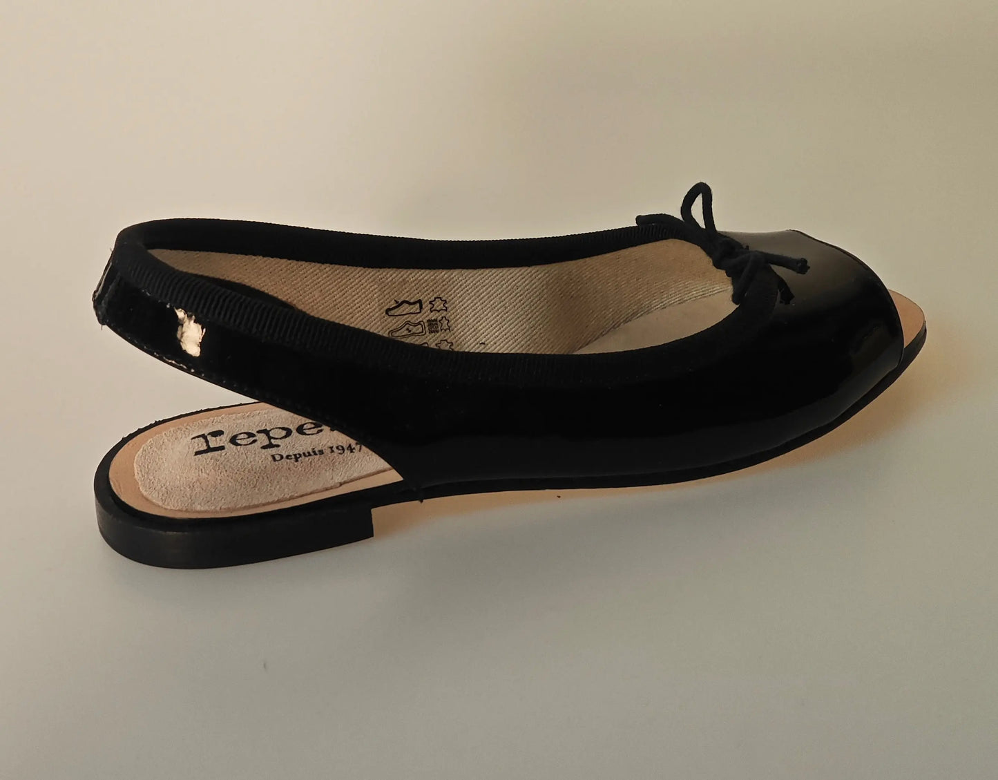 Ballerine slingback vernie noire de Repetto, avec un petit nœud décoratif sur le dessus.