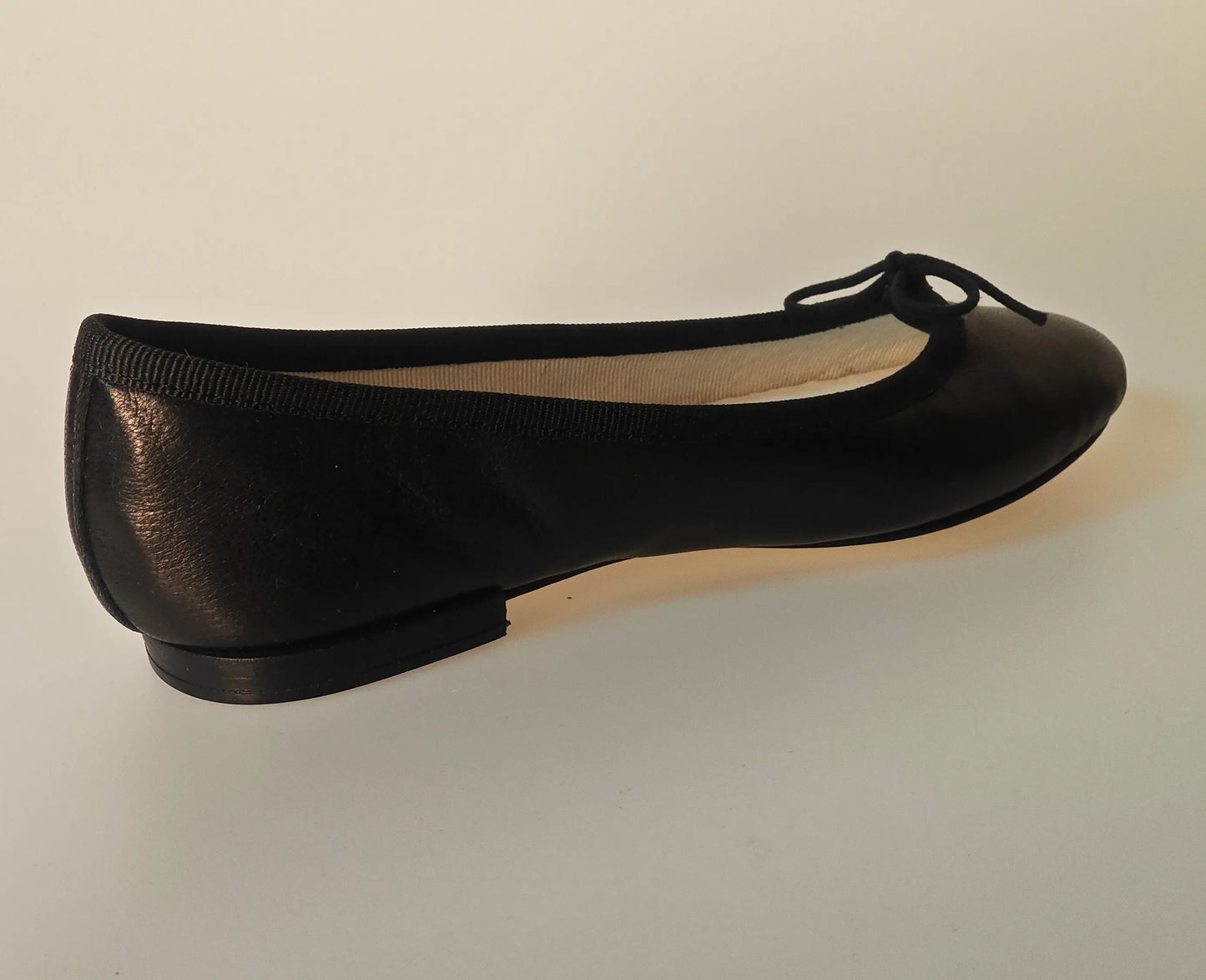 Ballerine noire en cuir véritable de Repetto, avec un petit nœud décoratif sur le dessus.
