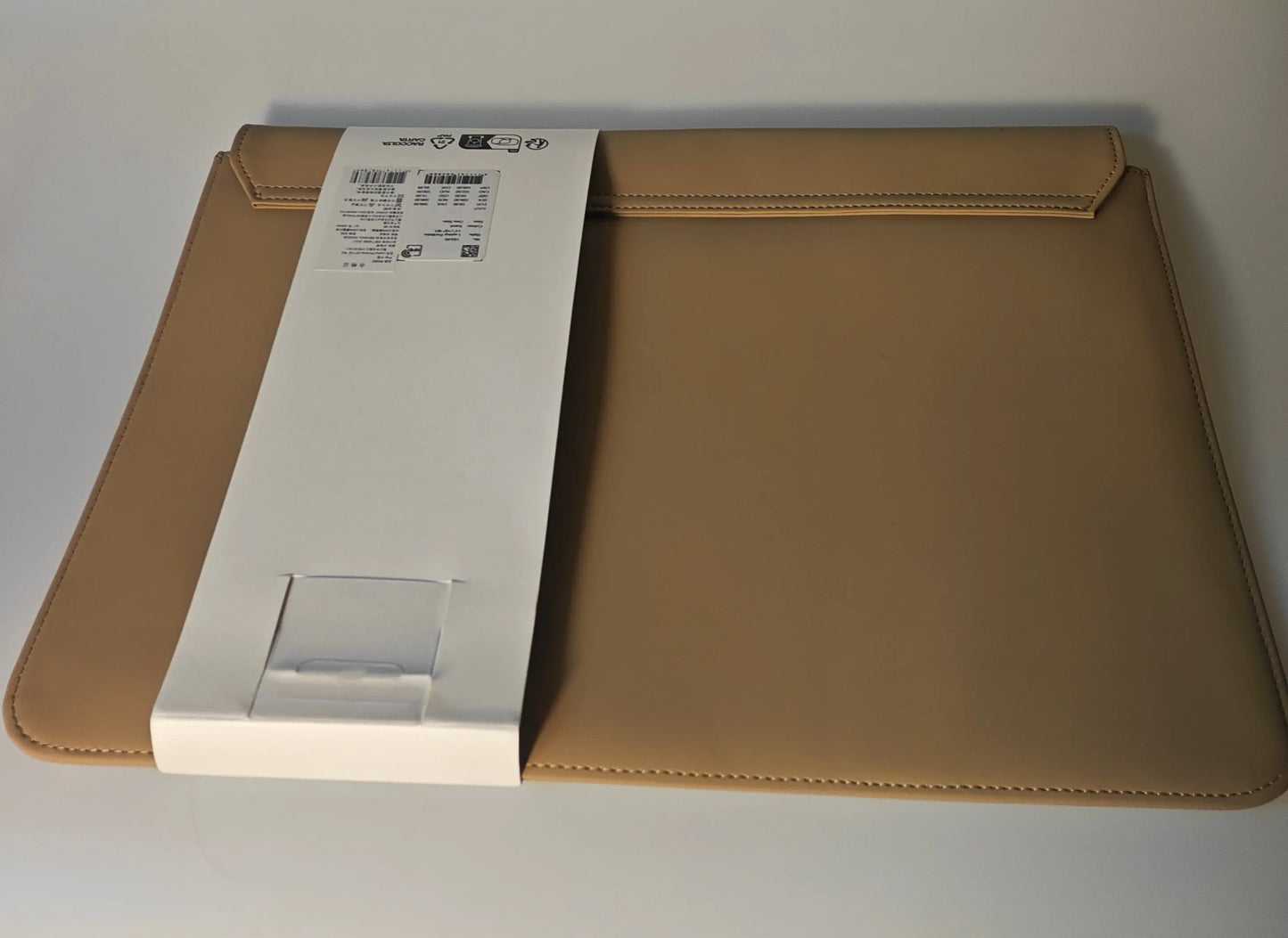 Housse d'ordinateur portable beige de Rains, avec fermeture à rabat et coutures sur le bord, présentée sur une surface claire.