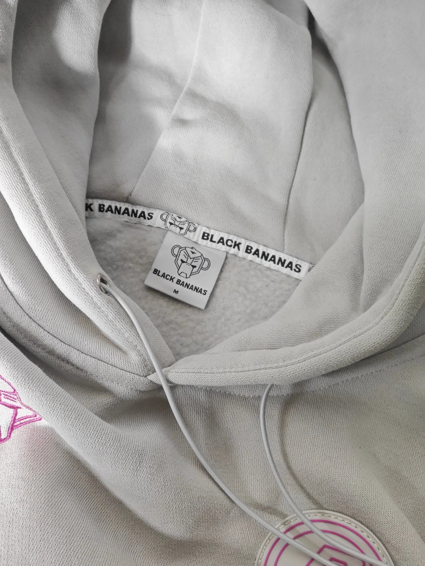 Sweat à capuche gris clair de Black Bananas, avec cordon de serrage et logo rose brodé.