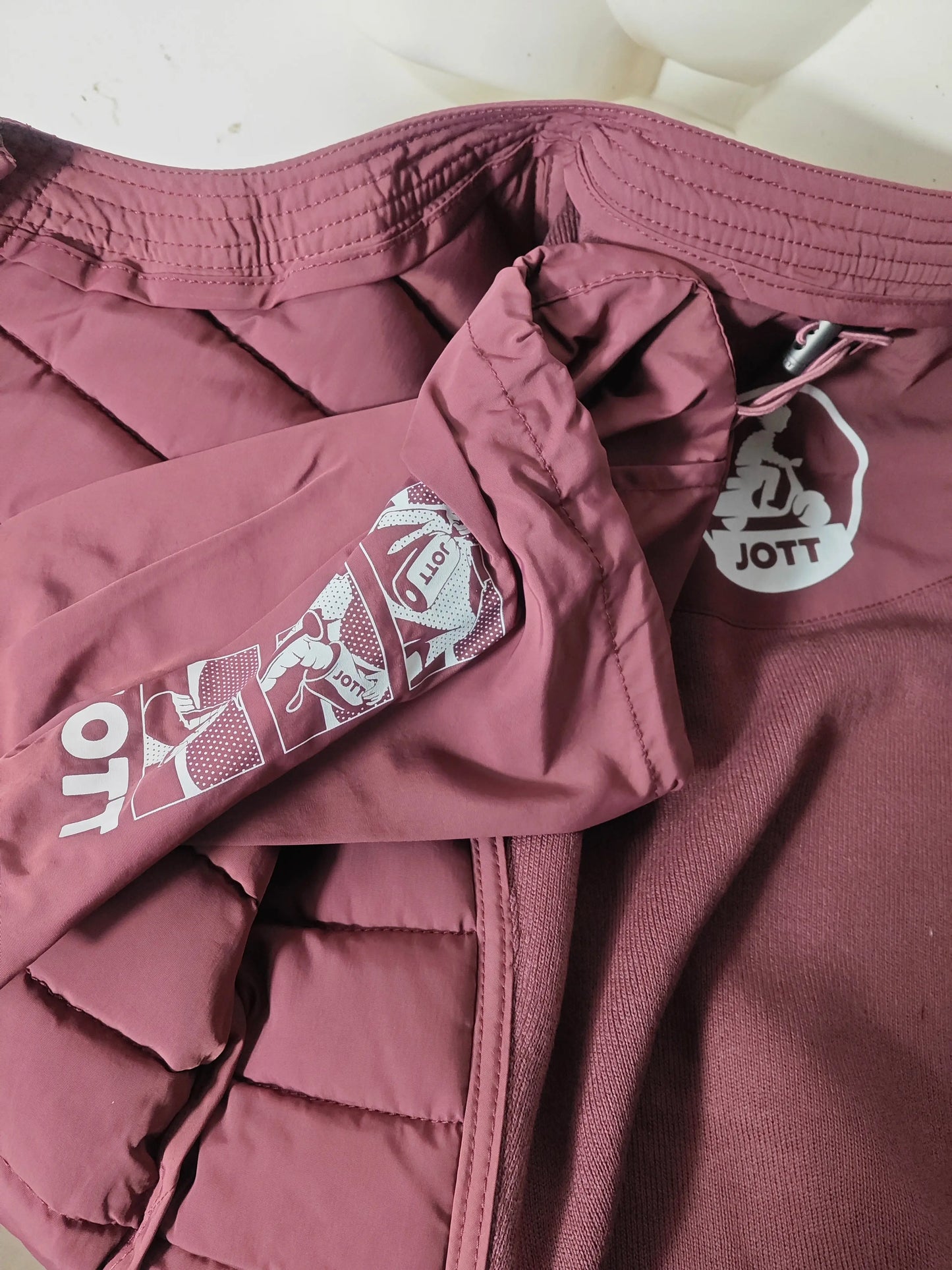 Veste bordeaux matelassée de Jott, avec logo et motifs imprimés sur la manche.