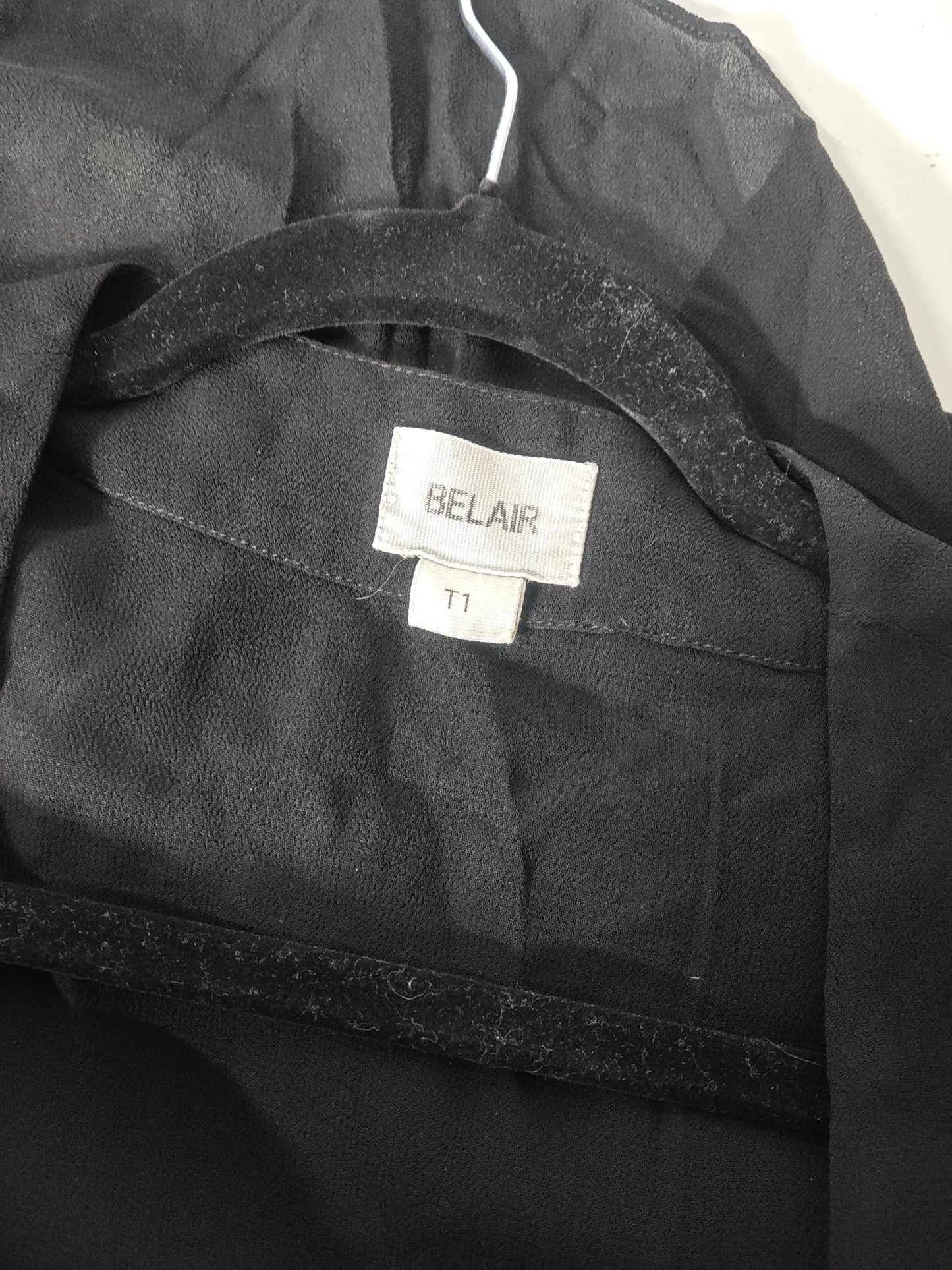 Blouse noire en dentelle et volants de Belair, sur un cintre en velours noir.