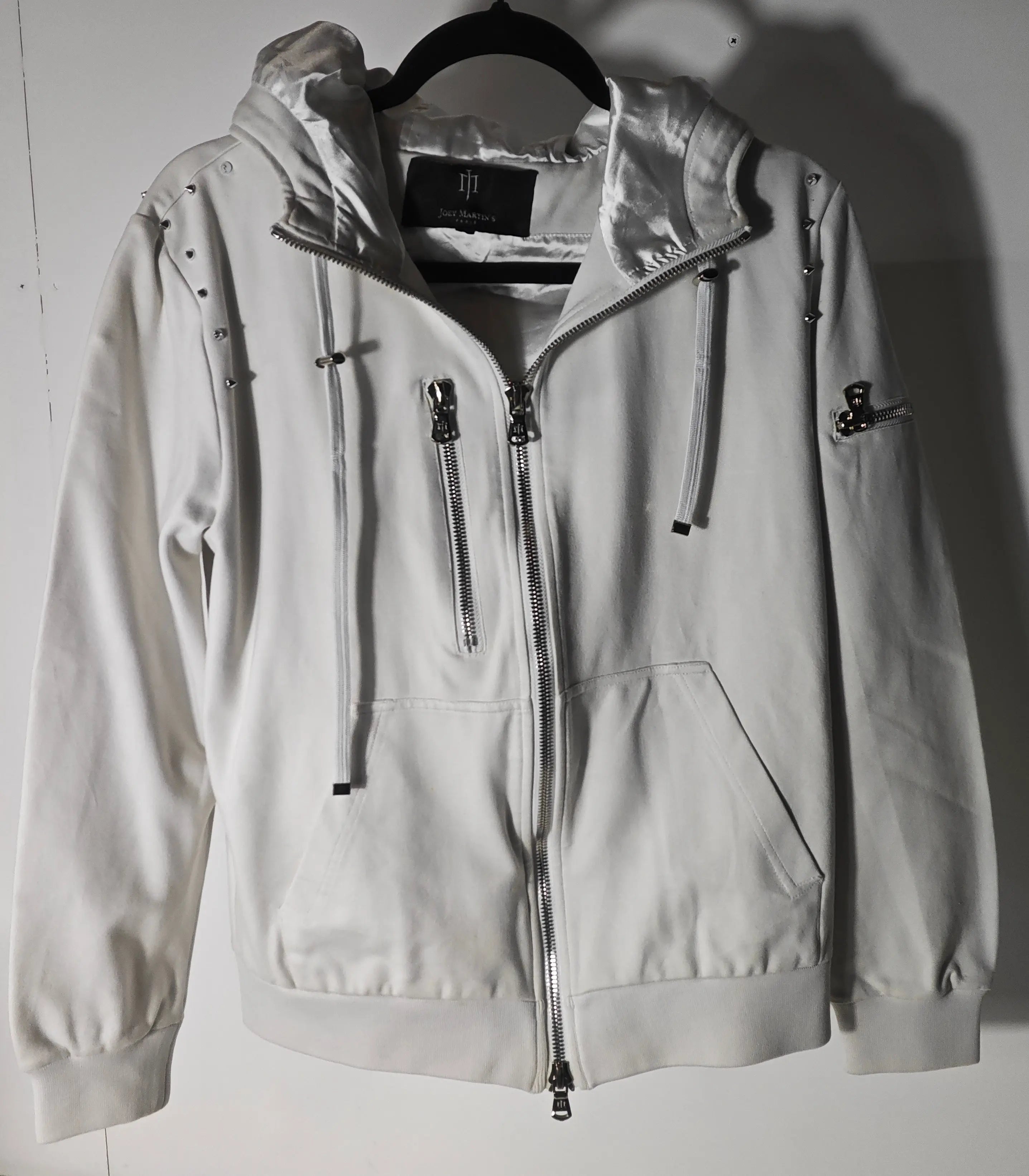 Veste à capuche blanche de Joey Martin’s Paris avec fermeture éclair, poches et détails cloutés.
