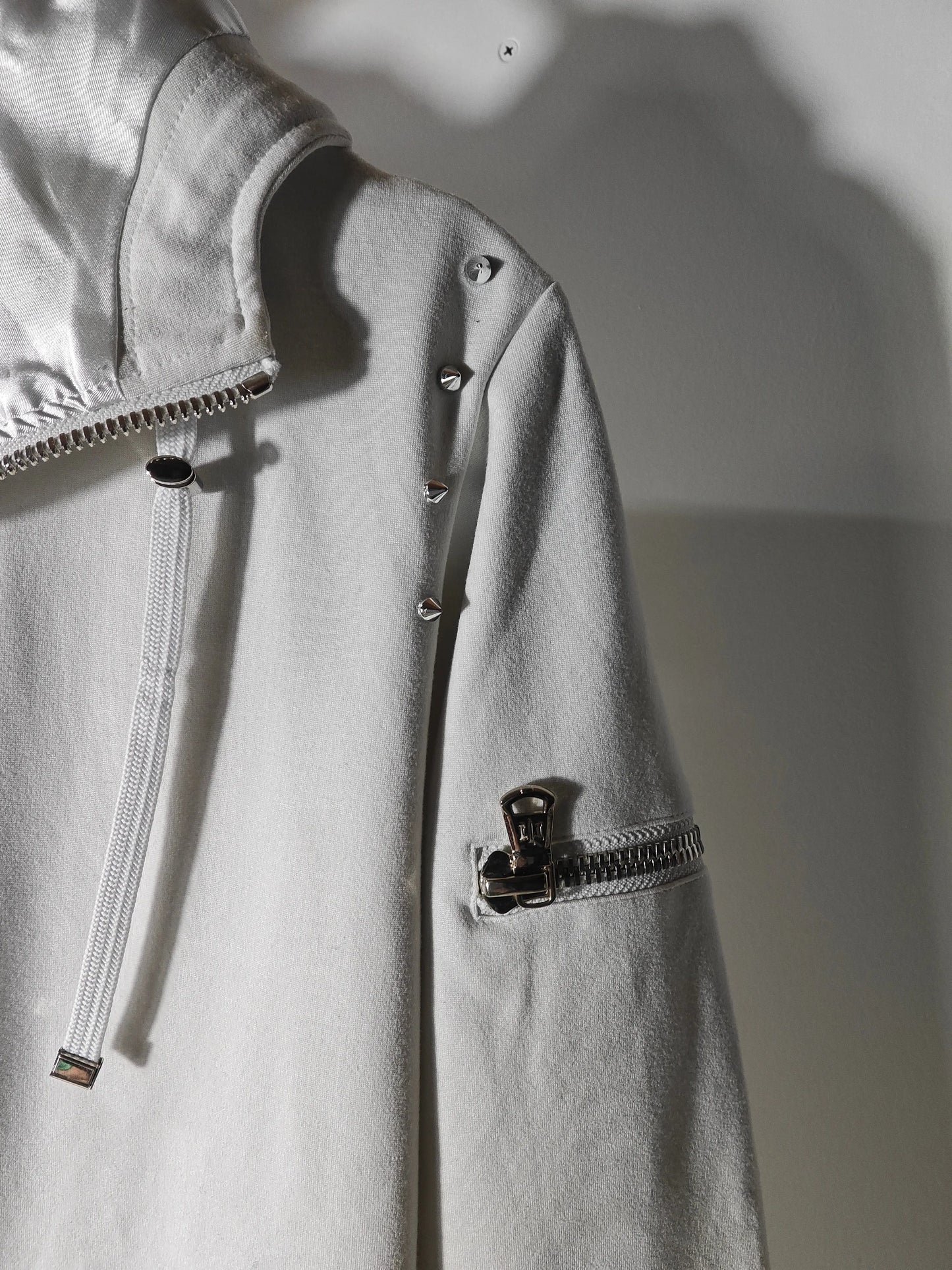 Veste à capuche blanche de Joey Martin’s Paris avec détails cloutés et fermeture éclair sur la manche.