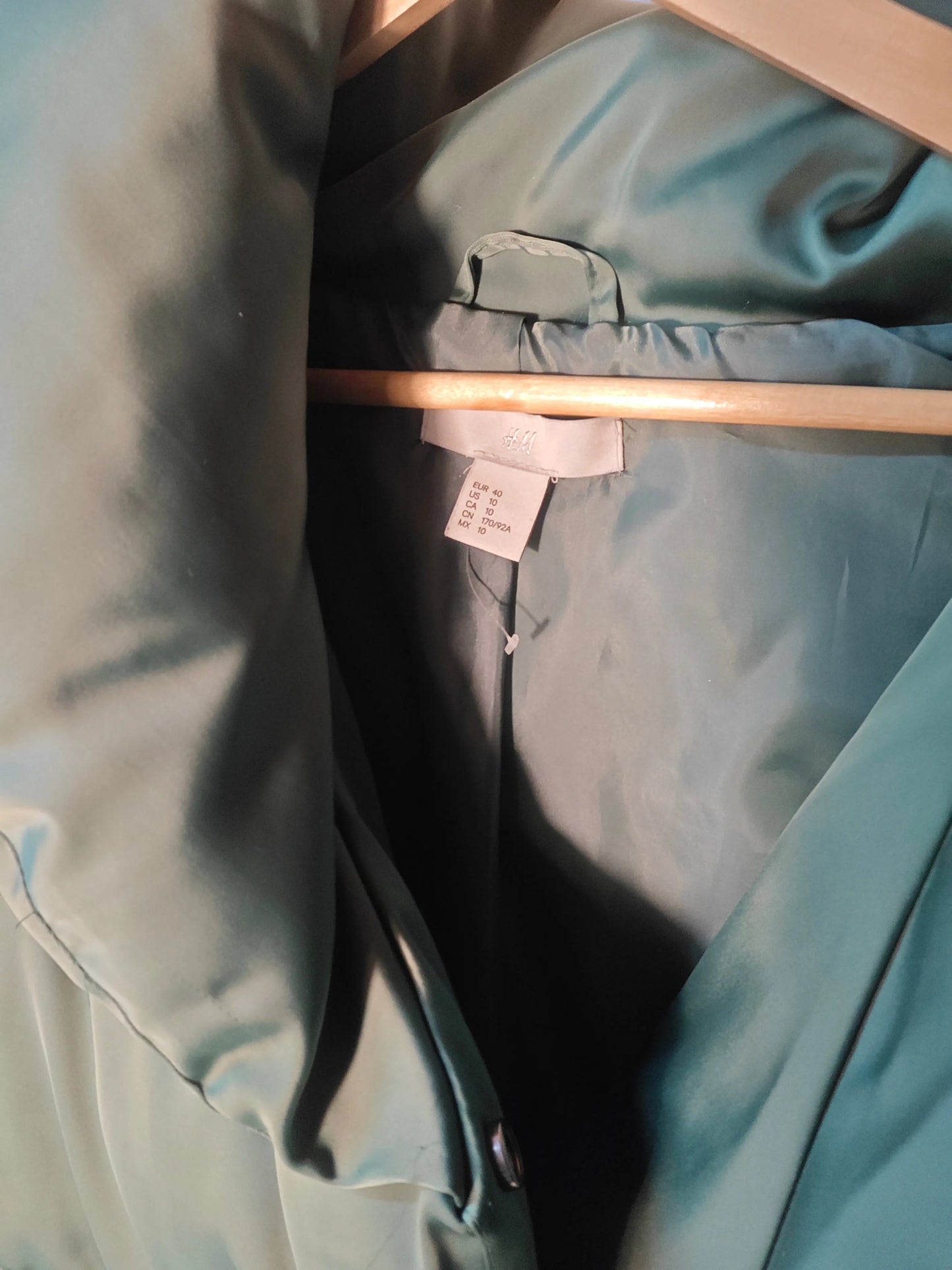 Doudoune verte par H&M, suspendue à un cintre en bois, avec une étiquette de taille visible.