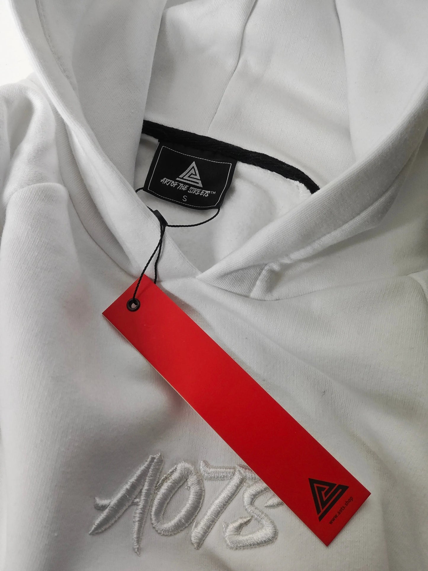Sweat à capuche blanc de AOTS, avec une broderie de marque sur le devant et étiquette rouge.