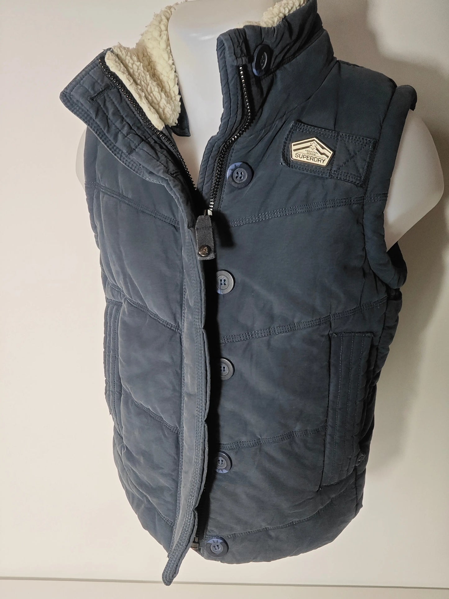 Doudoune sans manches bleue de Superdry avec doublure en peau de mouton et fermeture boutonnée partielle.