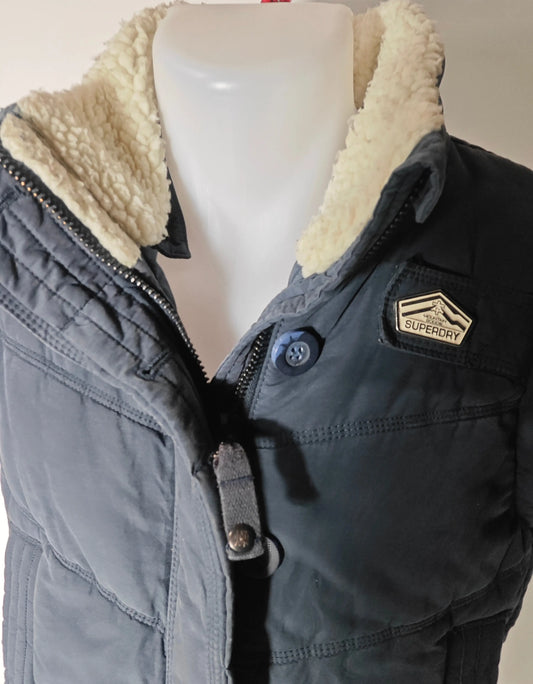Doudoune sans manches bleue de Superdry, avec col en fausse fourrure et écusson logo sur la poitrine.