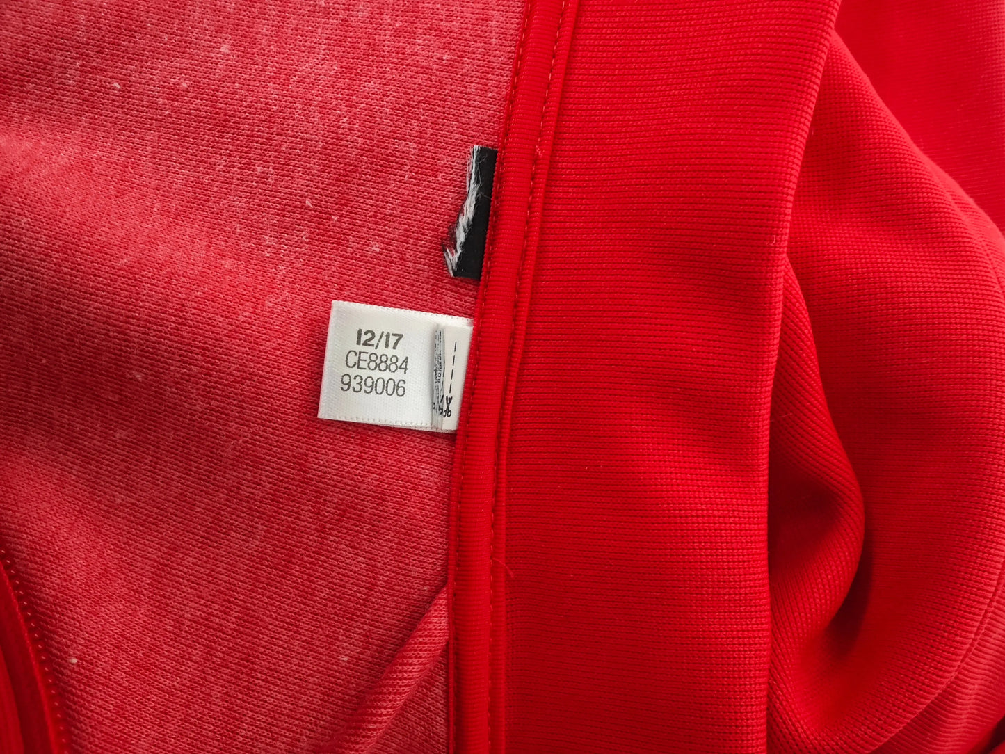 Veste de sport rouge par Adidas, montrant l'étiquette de taille avec des numéros de série.