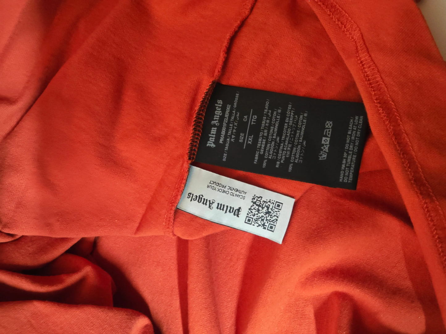 T-shirt orange oversize en coton, de Palm Angels, avec étiquettes d'entretien et QR code visibles.
