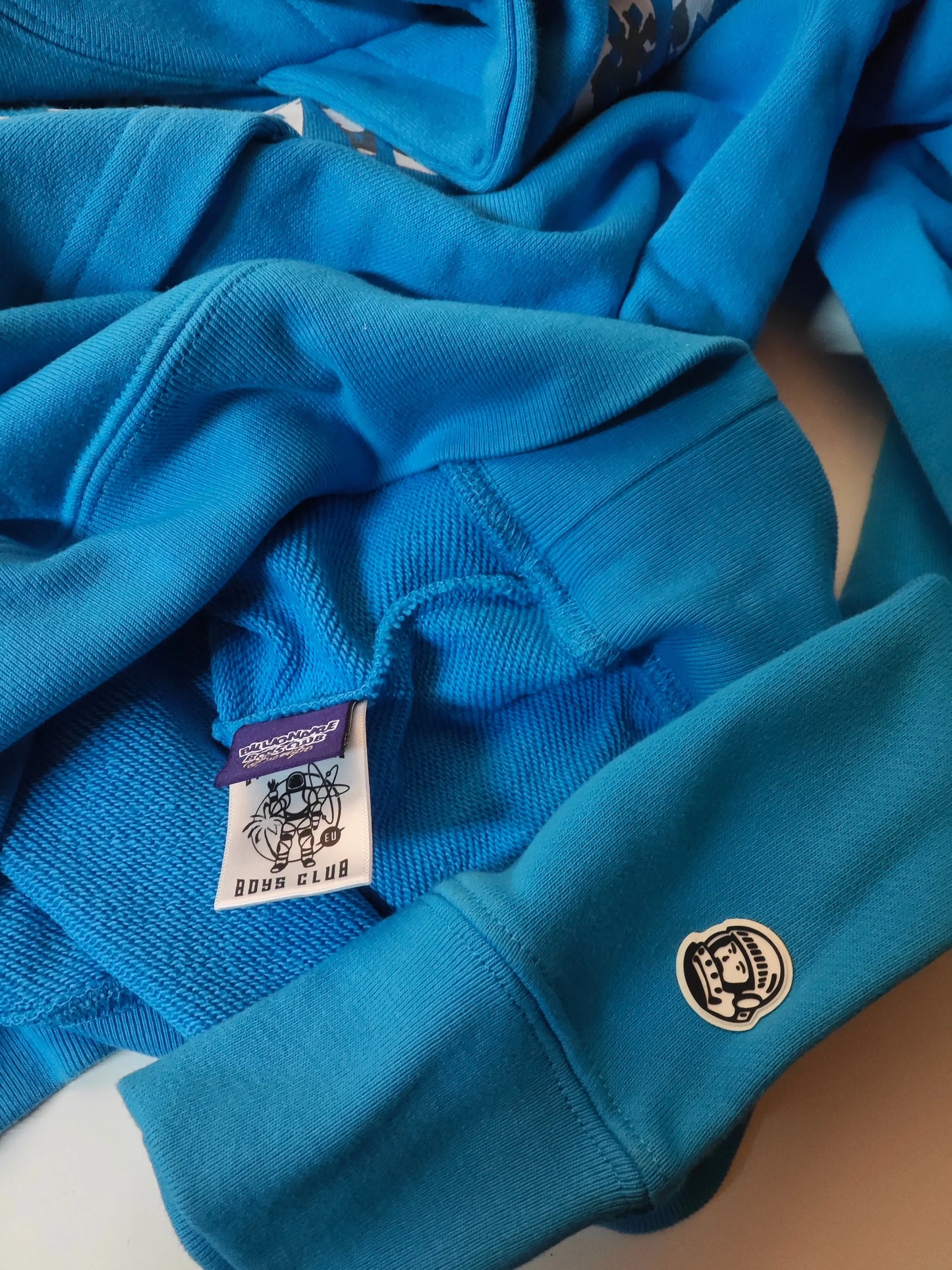 Sweat-shirt bleu de Billionaire Boys Club, avec étiquette logotypée et patch astronaute sur la manche.
