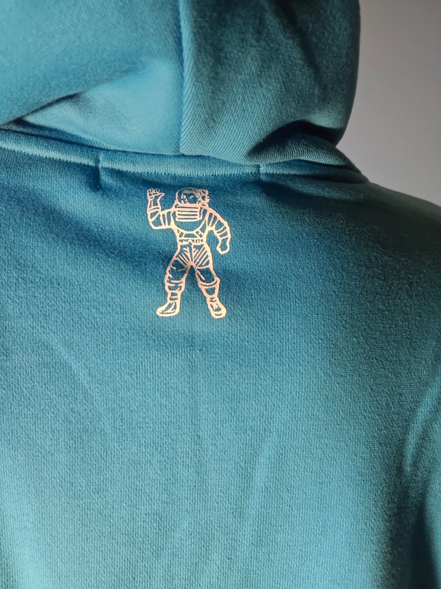 Sweat bleu par Billionaire Boys Club, orné d'un astronaute doré dans le dos, capuche visible.