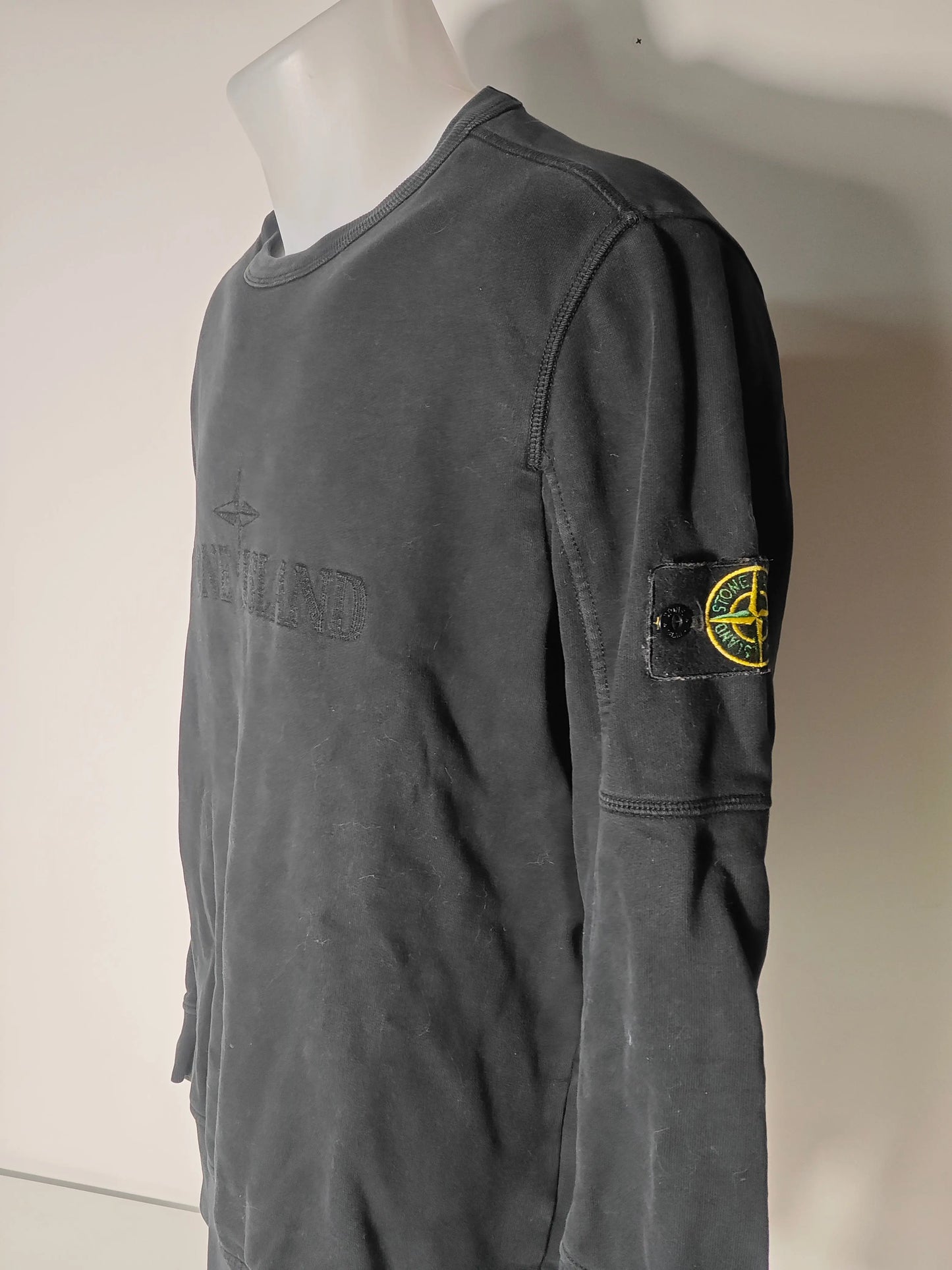 Sweat noir brodé ton-sur-ton de Stone Island, avec écusson logo sur la manche, présenté de côté sur un mannequin.