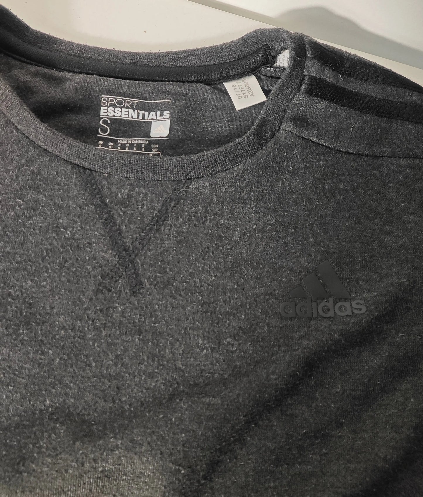 Sweat gris Sport Essentials de Adidas, avec logo ton sur ton et manches à trois bandes noires.