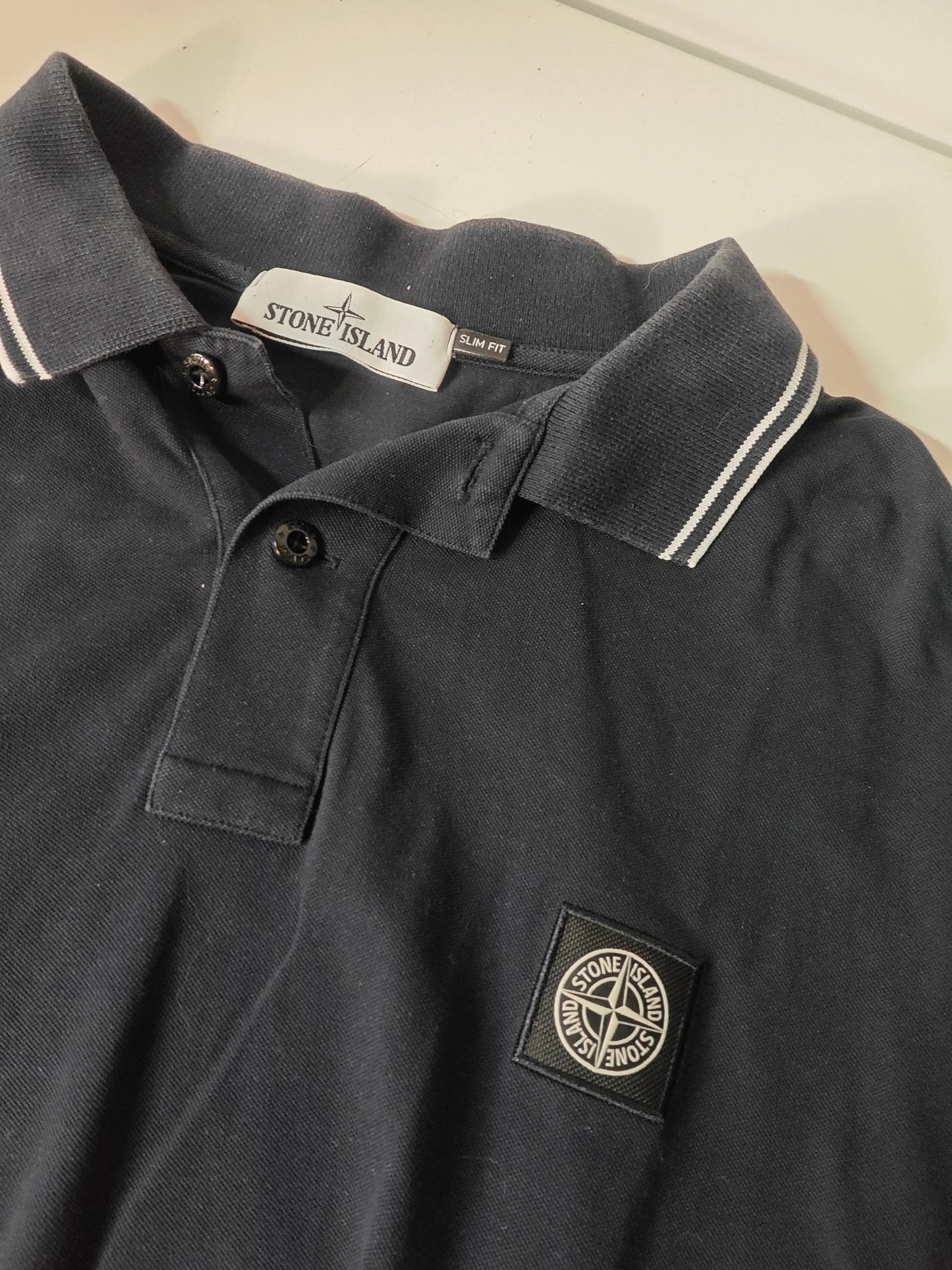Polo noir slim fit de Stone Island, avec col rayé blanc et patch logo sur le devant.