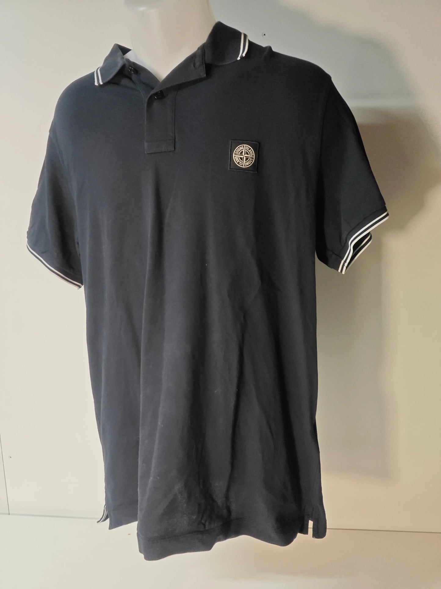 Polo noir à manches courtes de Stone Island, avec rayures blanches au col et aux manches, et écusson logo sur la poitrine.