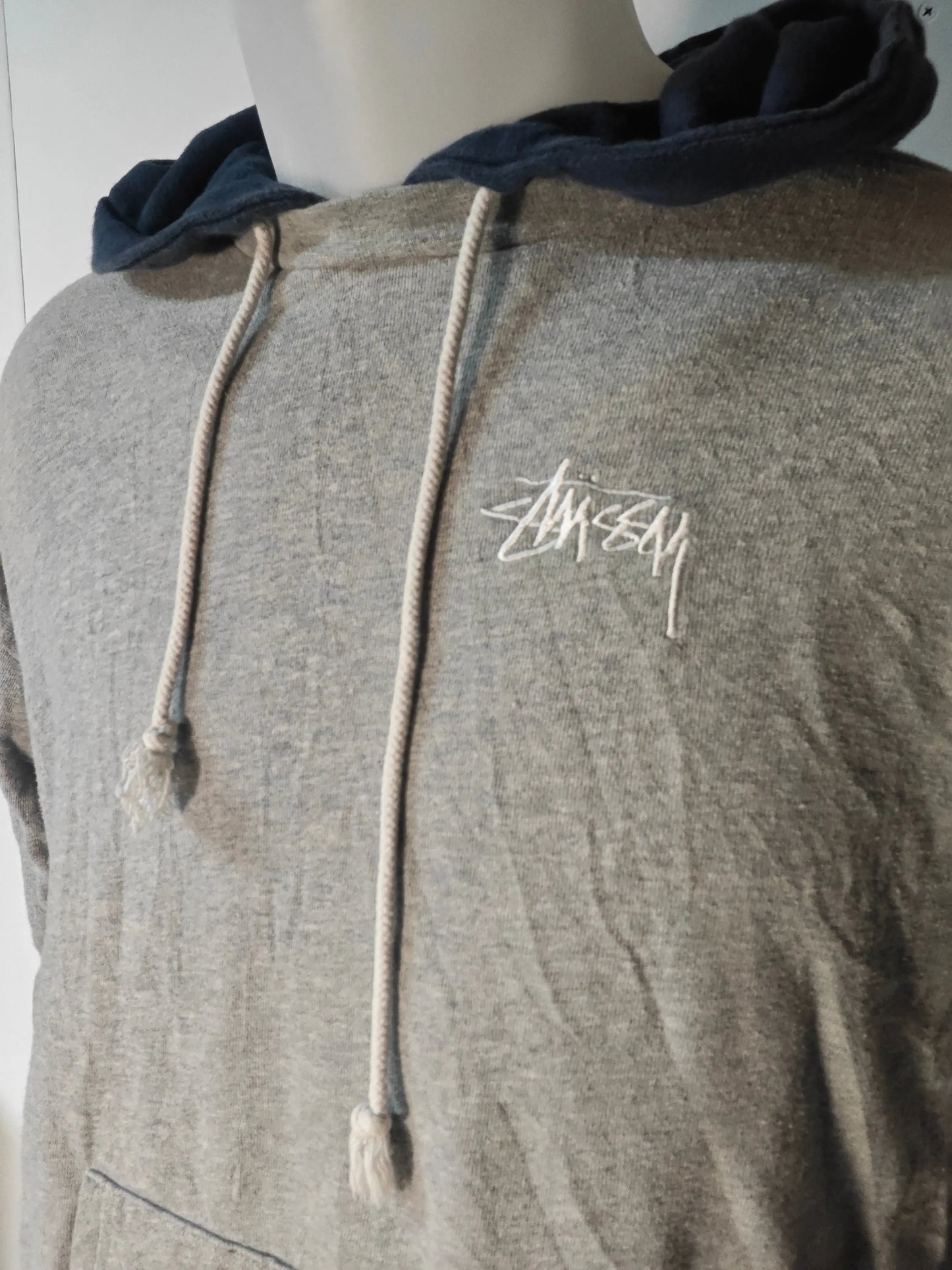 Sweat à capuche gris chiné de Stüssy, avec cordon et capuche bleu marine, logo brodé blanc.