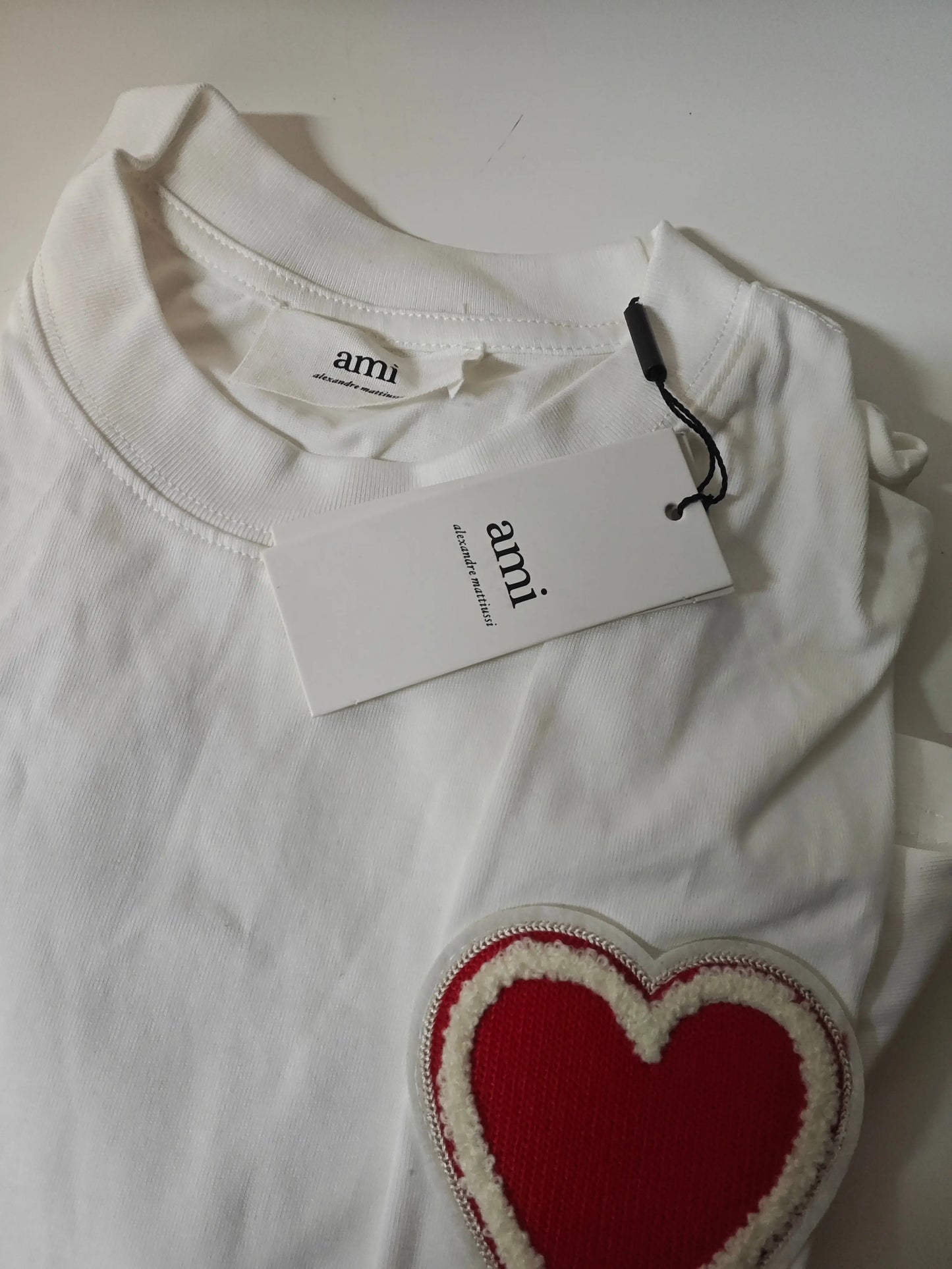 T-shirt blanc en coton AMI Paris avec patch cœur bouclette rouge et détails blancs.