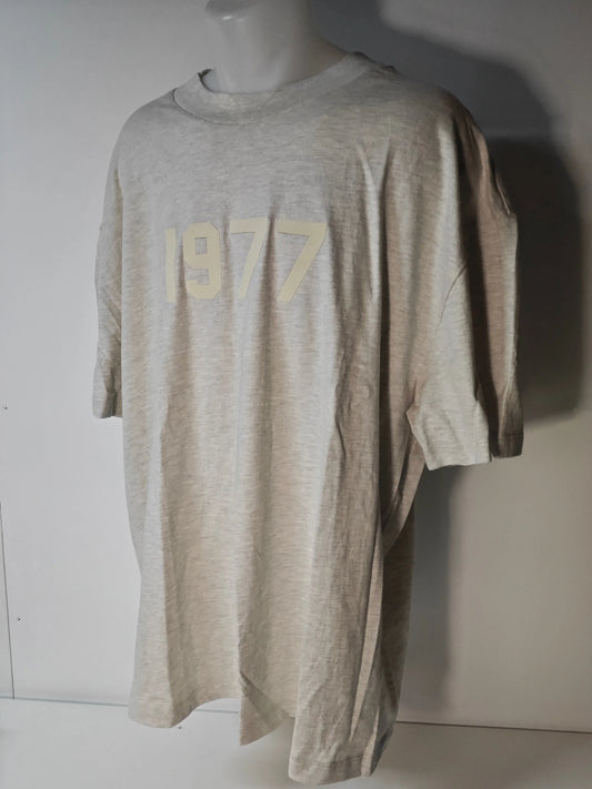 T-shirt beige chiné ESSENTIALS par Fear of God avec l'inscription « 1977 » sur le devant.