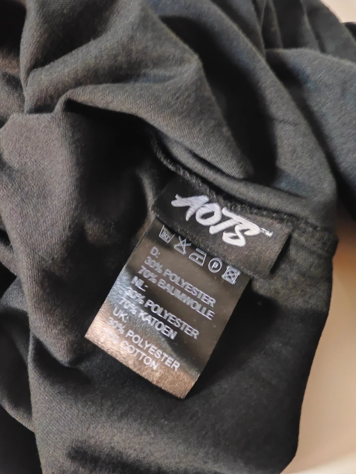 T-shirt Art of the Streets noir de AOTS, avec étiquette d'entretien visible.