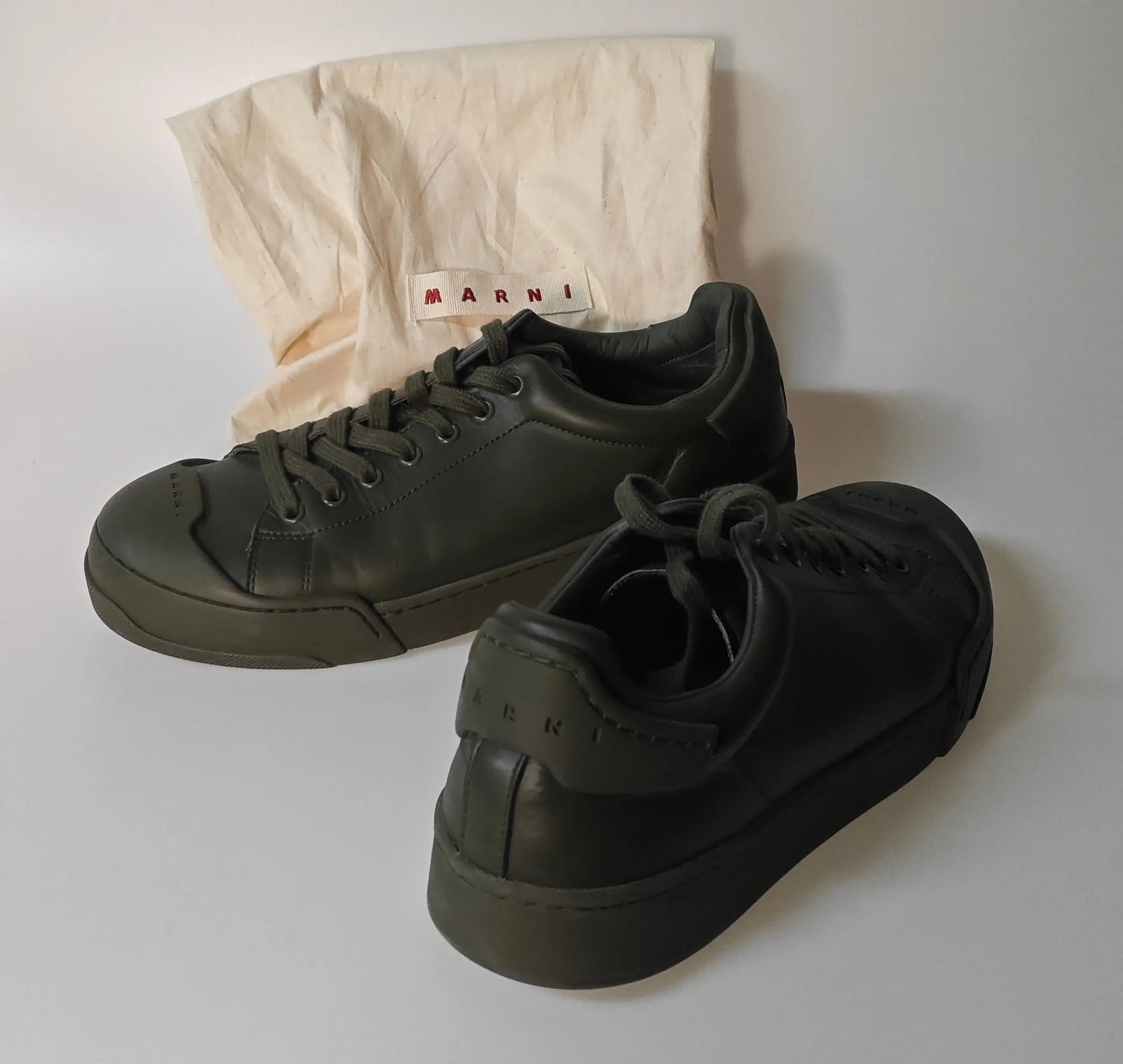 Baskets vertes kaki de Marni, avec la mention de la marque sur la languette arrière, posées à côté de leur housse de rangement.