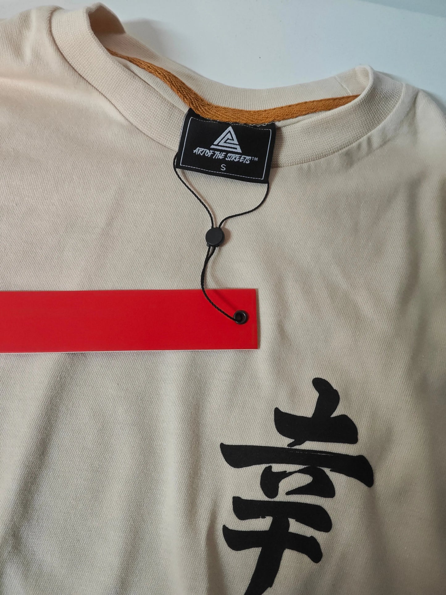 T-shirt beige à manches courtes de AOTS, avec un motif rouge horizontal et un motif calligraphique noir.