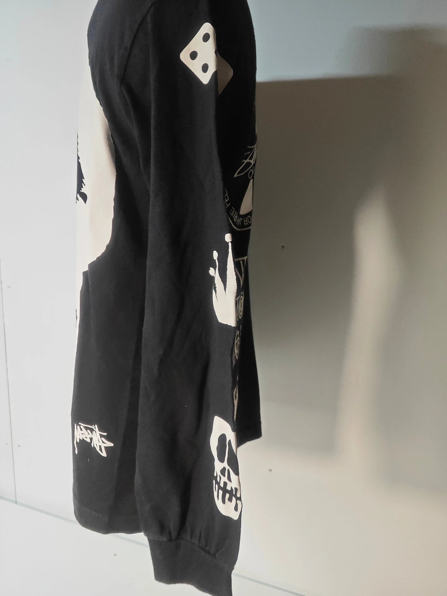 T-shirt noir à manches longues de Stüssy, orné de motifs graphiques blancs sur la manche.