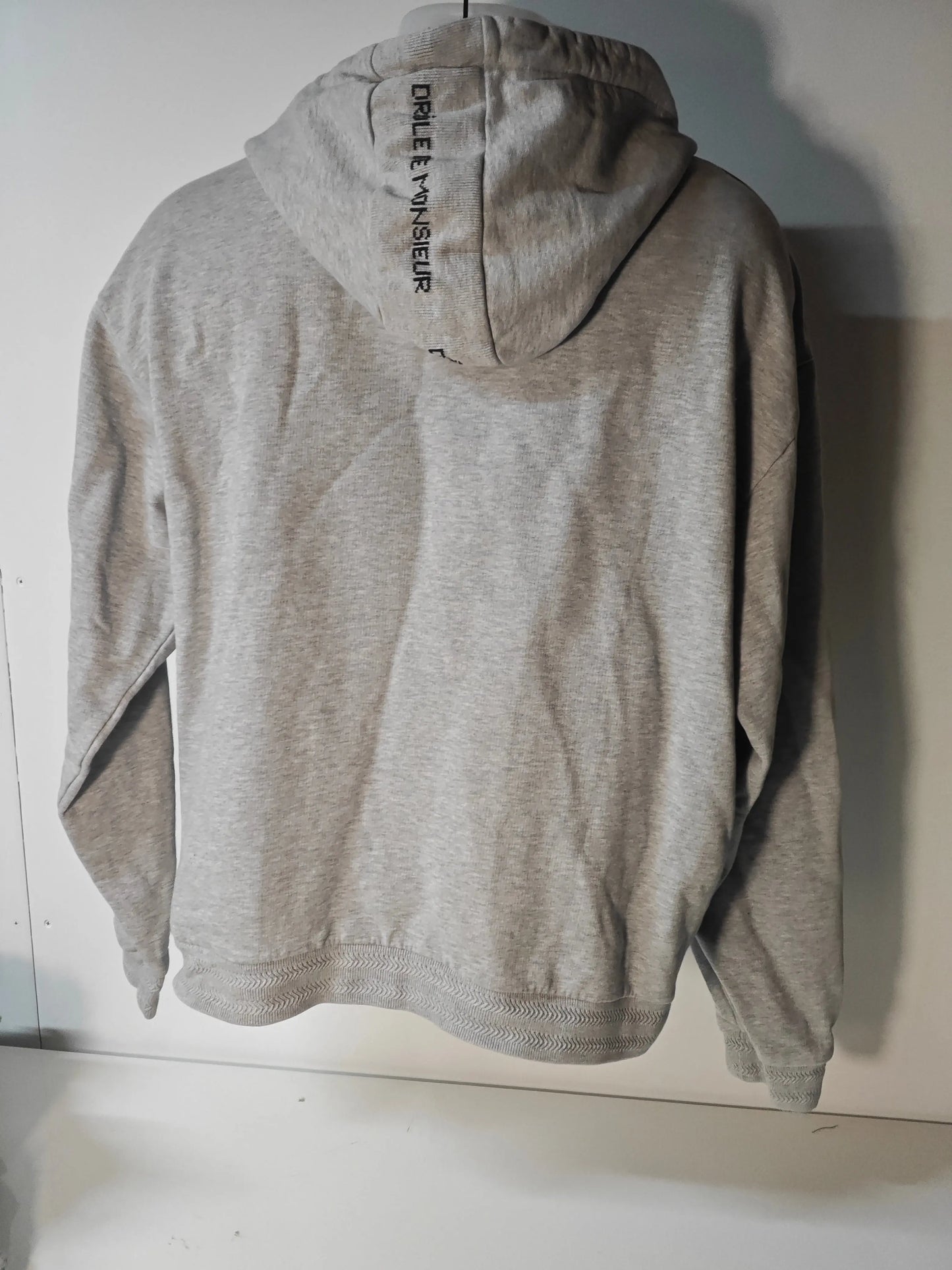 Sweat à capuche gris chiné de Drôle de Monsieur, avec le logo imprimé verticalement sur la capuche, vu de dos.