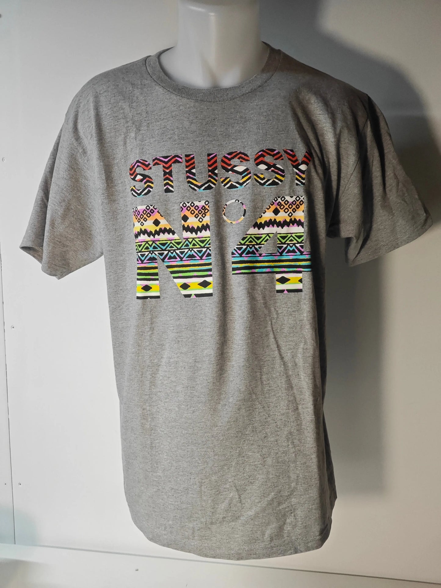 T-shirt gris Stüssy, avec un imprimé multicolore des lettres et chiffres sur le devant.