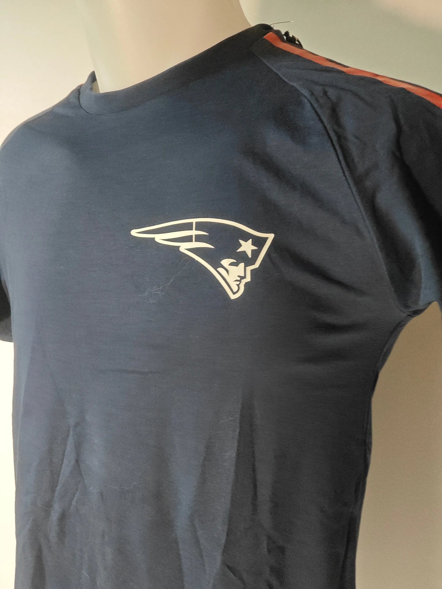 T-shirt bleu marine des New England Patriots de New Era, avec rayures orange sur les épaules et logo sur le devant.