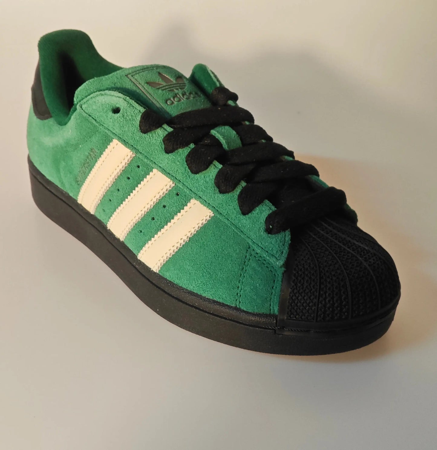 Baskets Superstar en daim vert et noir par Adidas, avec les trois rayures blanches sur le côté.