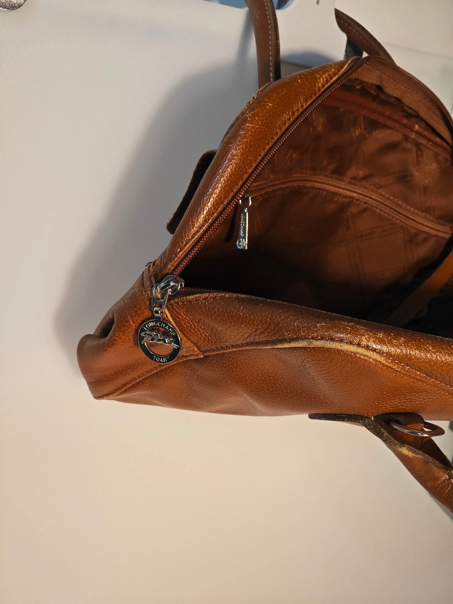 Sac à main en cuir marron, de Longchamp, avec fermeture éclair argentée et logo distinctif.
