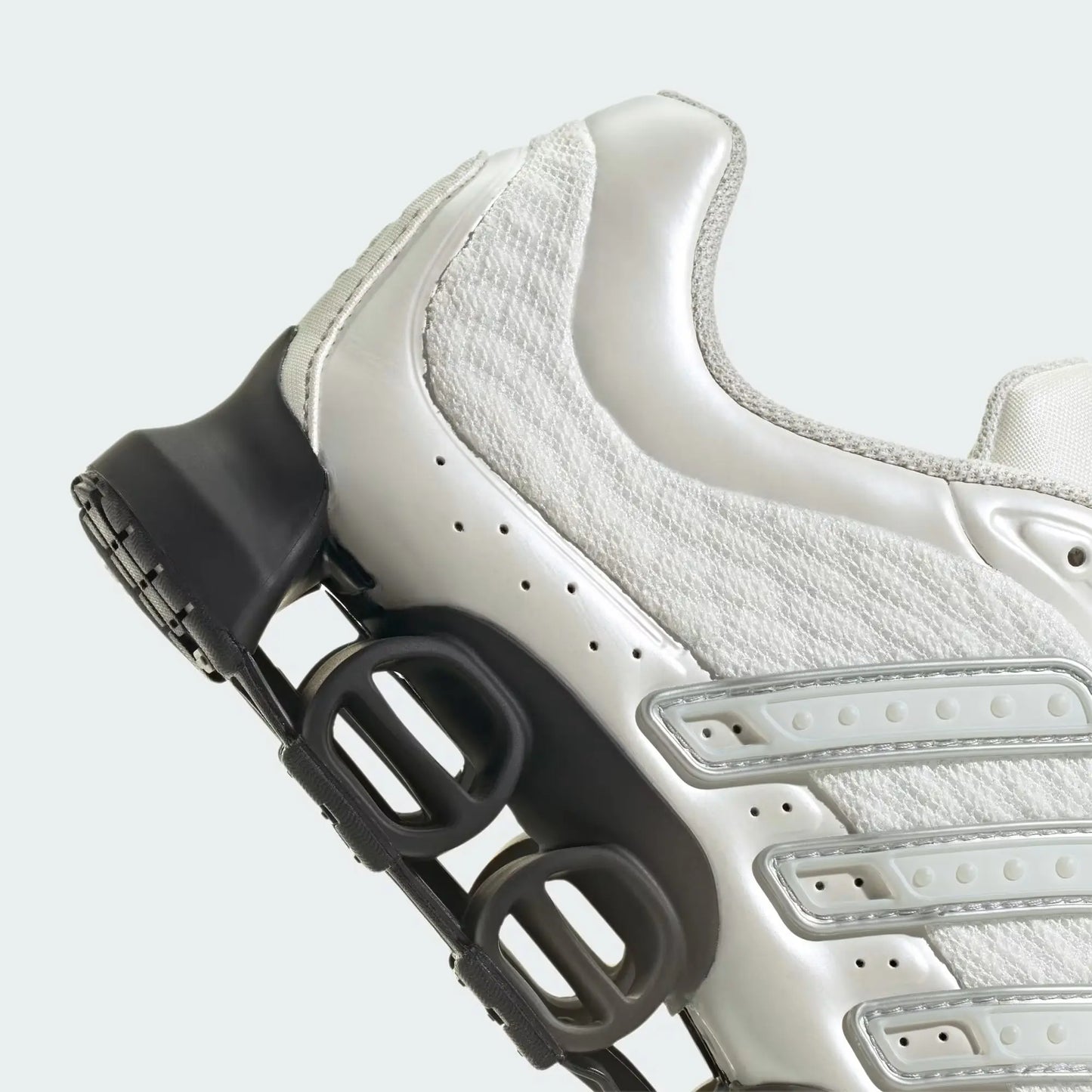 Chaussure de sport blanche par Adidas, avec des accents argentés et semelle noire à ressorts.