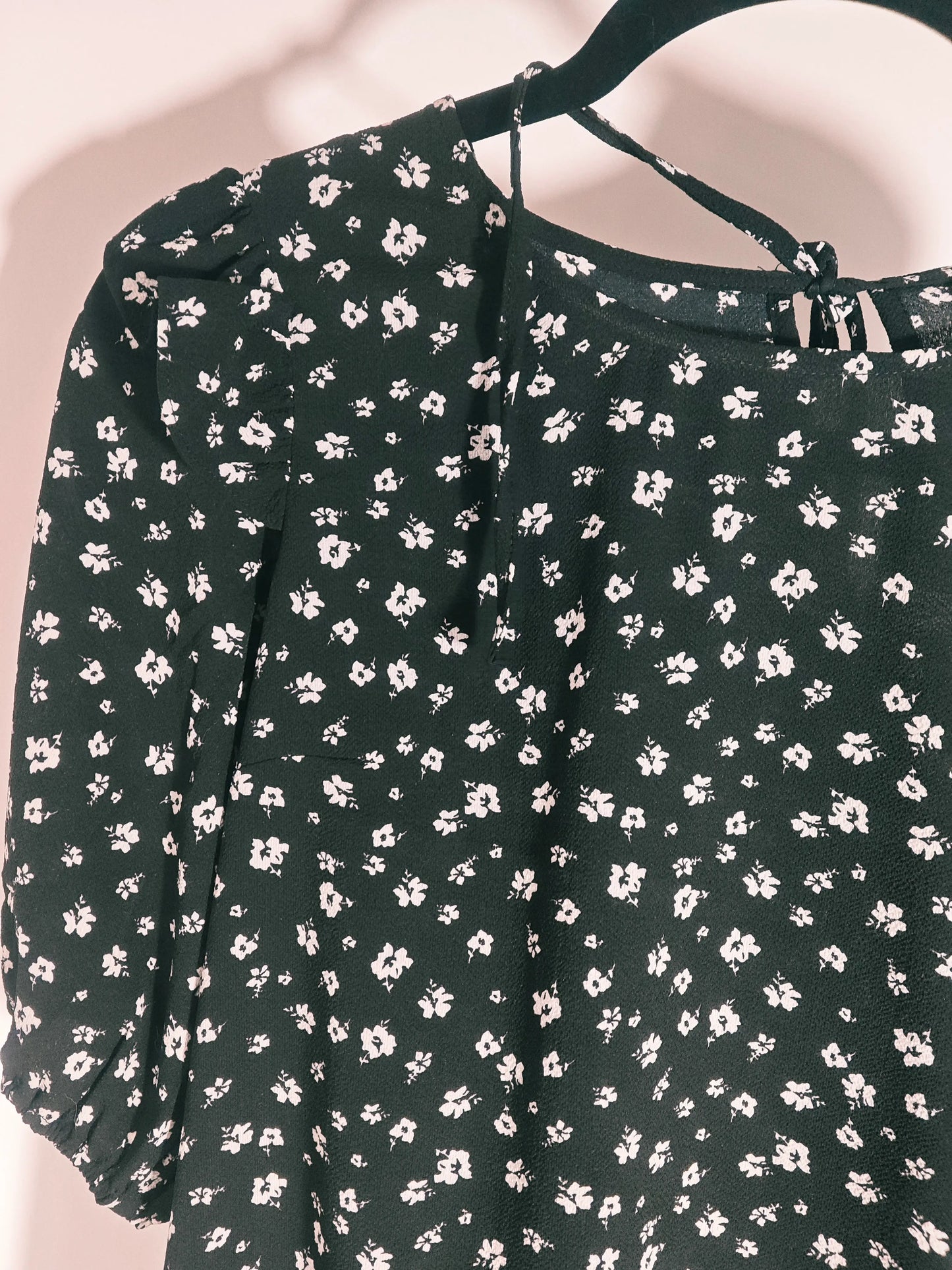 Robe fleurie noire H&M, à motif floral blanc, suspendue à un cintre noir.
